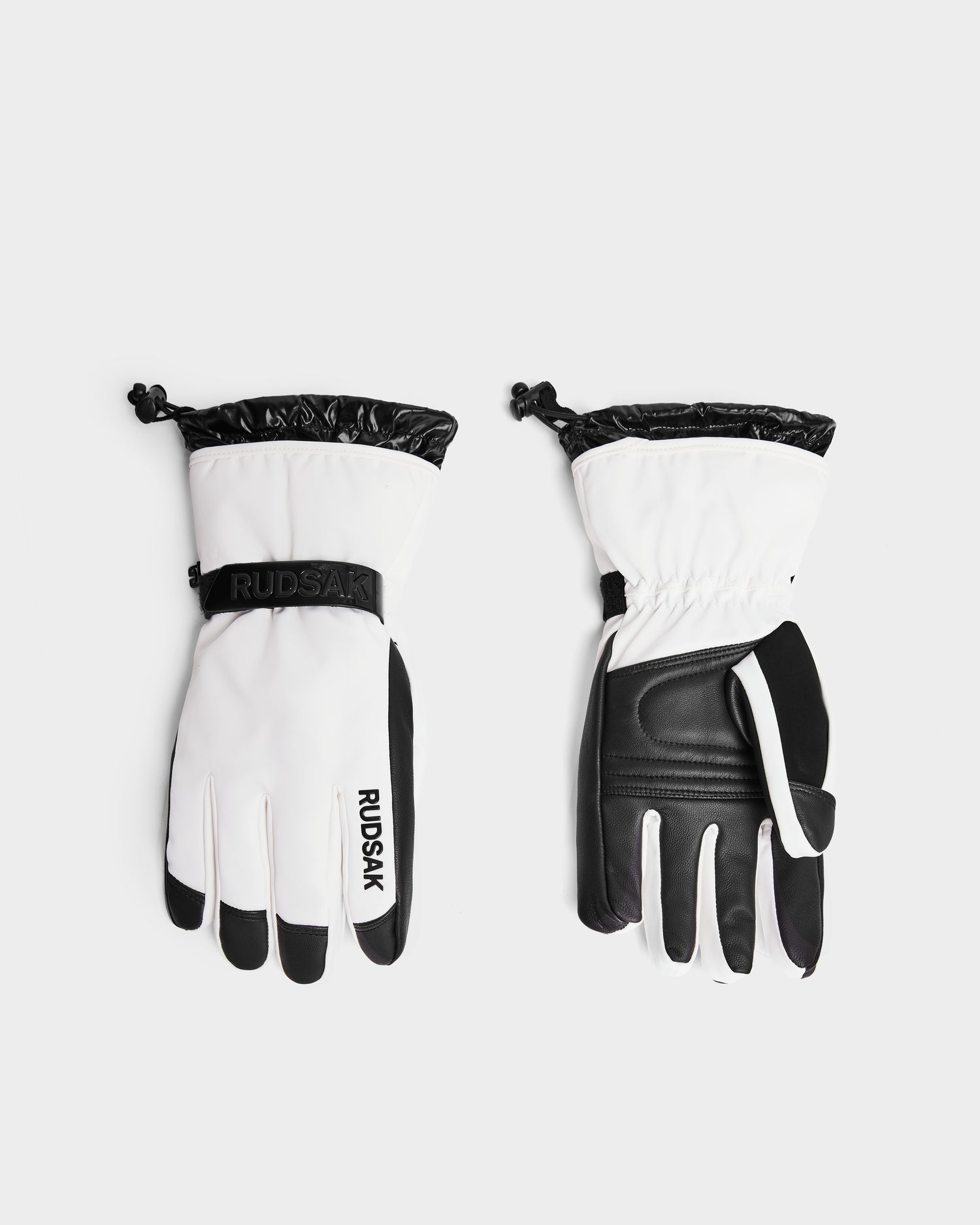A pair of Rudsak APLEN - 6424505 Optic White ski gloves in white and black, shown front and back with adjustable wrist straps, drawstring cuffs, and waterproof zippers, displayed on a plain light background.