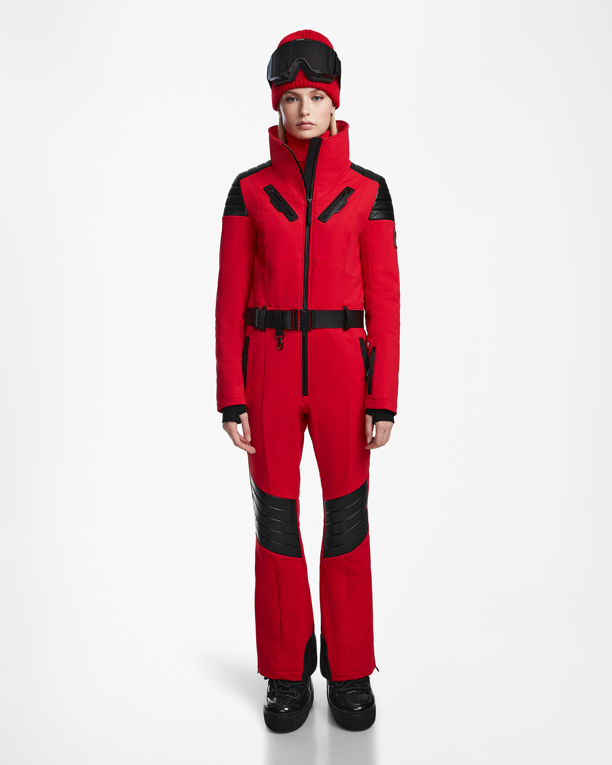A person faces forward wearing the Rudsak ARLEY - 8124717 Flame Red fitted women’s ski suit with black accents, black gloves, boots, and ski goggles on their head. Set against a plain white background. Features integrated RECCO rescue technology.