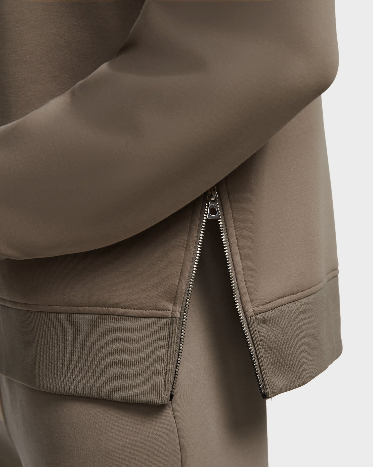 Close-up of the Rudsak AVERY - 9524505 Cement M: a unisex taupe mock neck zip-up sweater with ribbed cuffs and hem, shown with its metallic zipper partially undone to reveal the inner fabric.