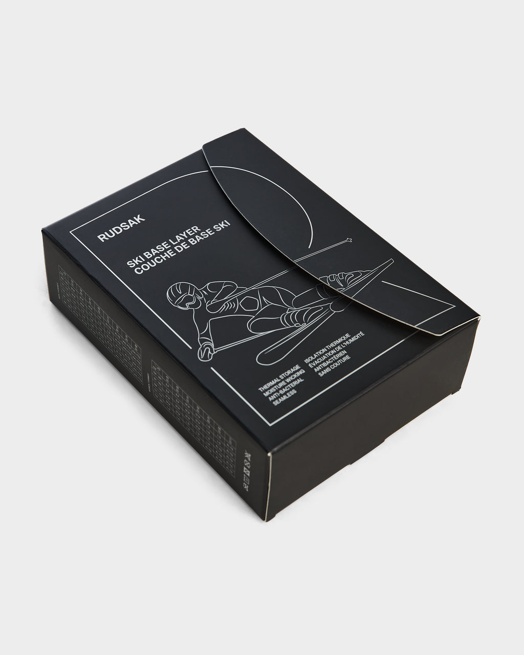 A black Rudsak box labeled CARRIE - 8524619 Black shows a white line drawing of a skier on the lid, hinting at the womens stretch set inside—ideal for thermal performance as a ski base layer. The box sits partially open on a white background.