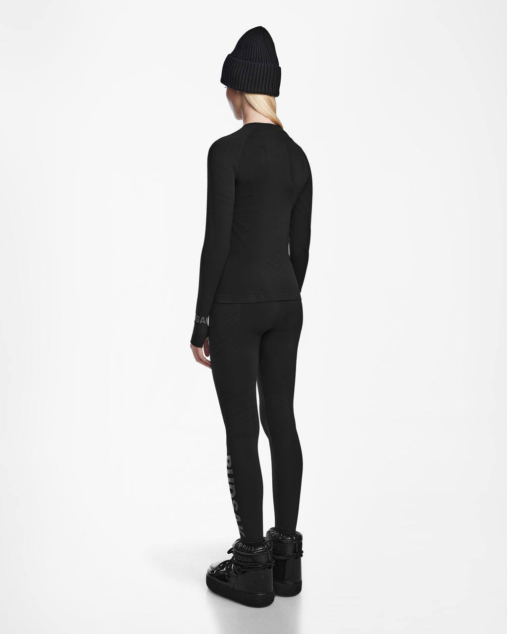 A person faces away, wearing the Rudsak CARRIE - 8524619 Black women’s stretch set with a black beanie and boots, set against a plain white background.