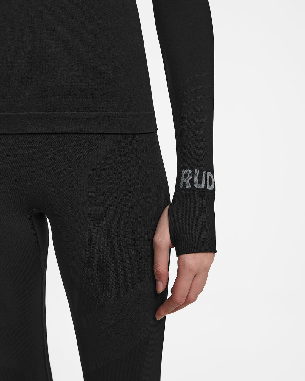 A person is wearing the Rudsak CARRIE - 8524619 Black women’s stretch set with long sleeves and thumb holes, displaying RUD in gray near the wrist. Only the lower torso and arm are visible against a white background, highlighting ski underlayer performance.