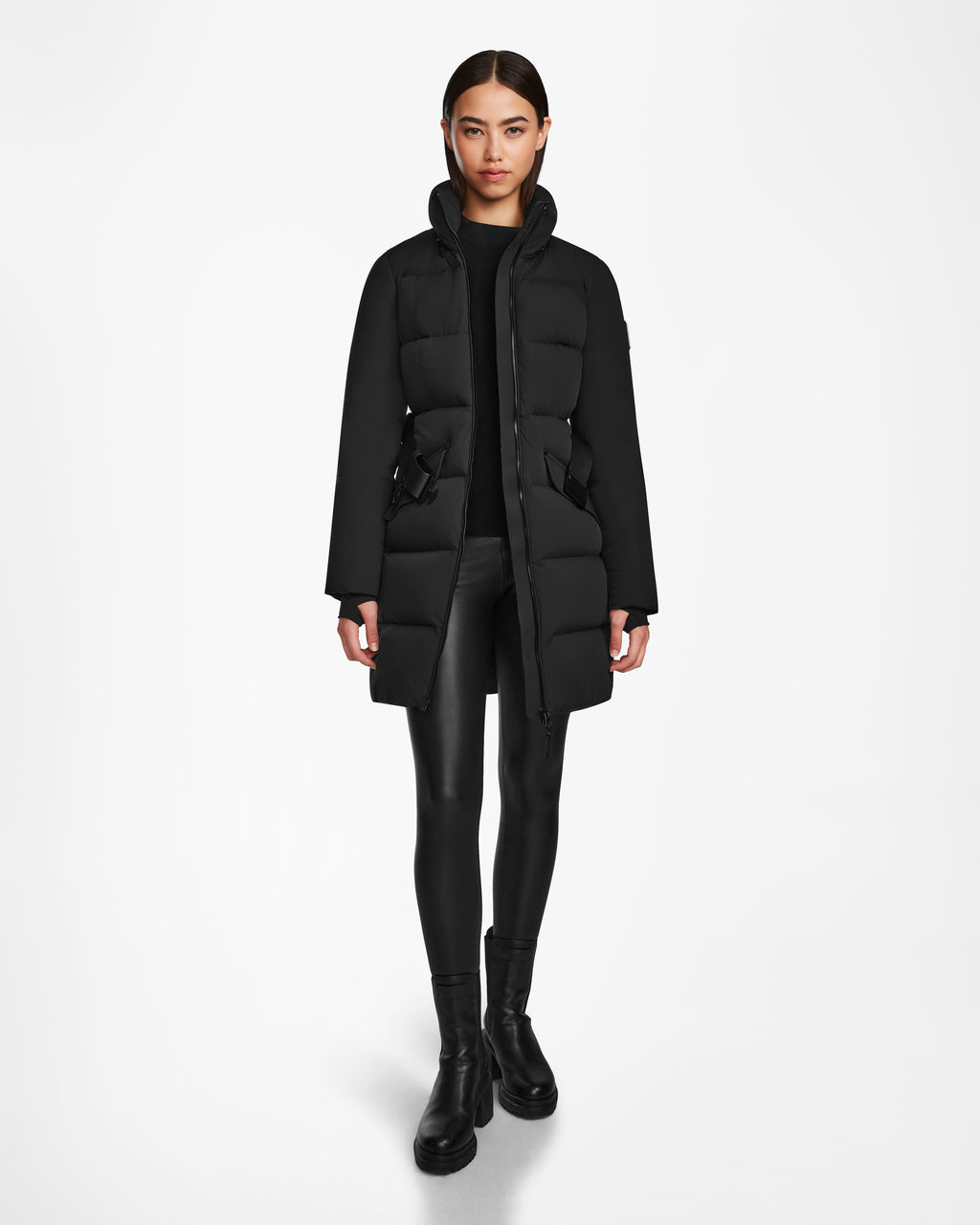 A woman stands facing forward wearing the Rudsak CAT - 8124584 Black quilted down puffer, black leggings, and black boots against a plain white background.