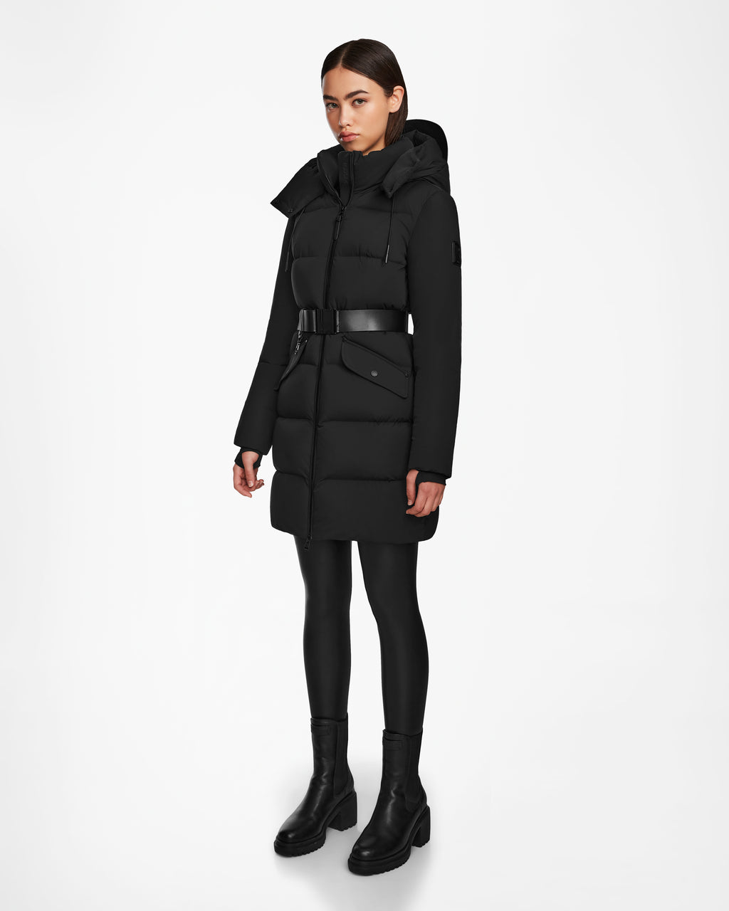 A woman wears the Rudsak CAT - 8124584 Black mid-length puffer coat with RDS-certified down, black leggings, and black boots, standing against a plain white background.