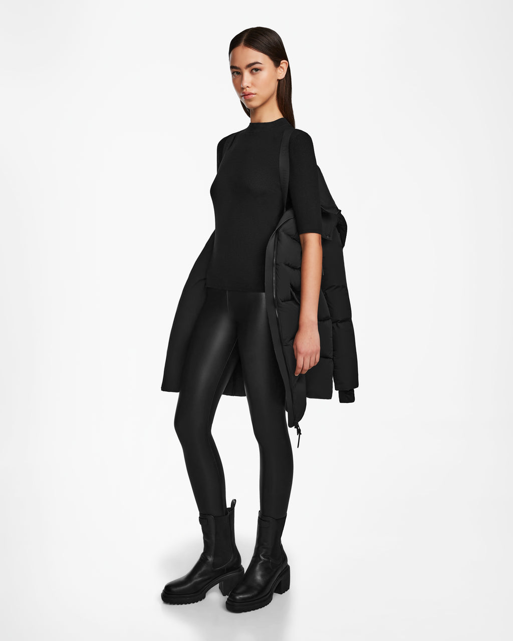 A woman in black clothing wears the Rudsak CAT - 8124584 Black, a mid-length puffer with a sleek silhouette and RDS-certified down fill for comfort and warmth.