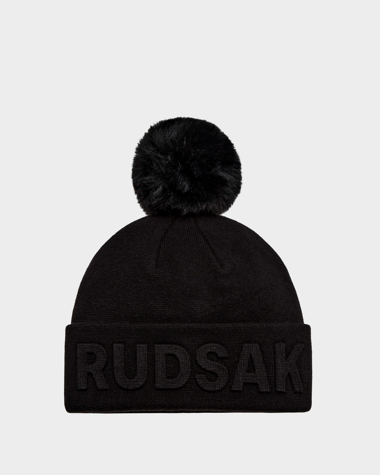 The Rudsak CERRY - 9423508 Black is a unisex knit tuque with a large removable black pom-pom and bold RUDSAK embroidery on the folded brim.