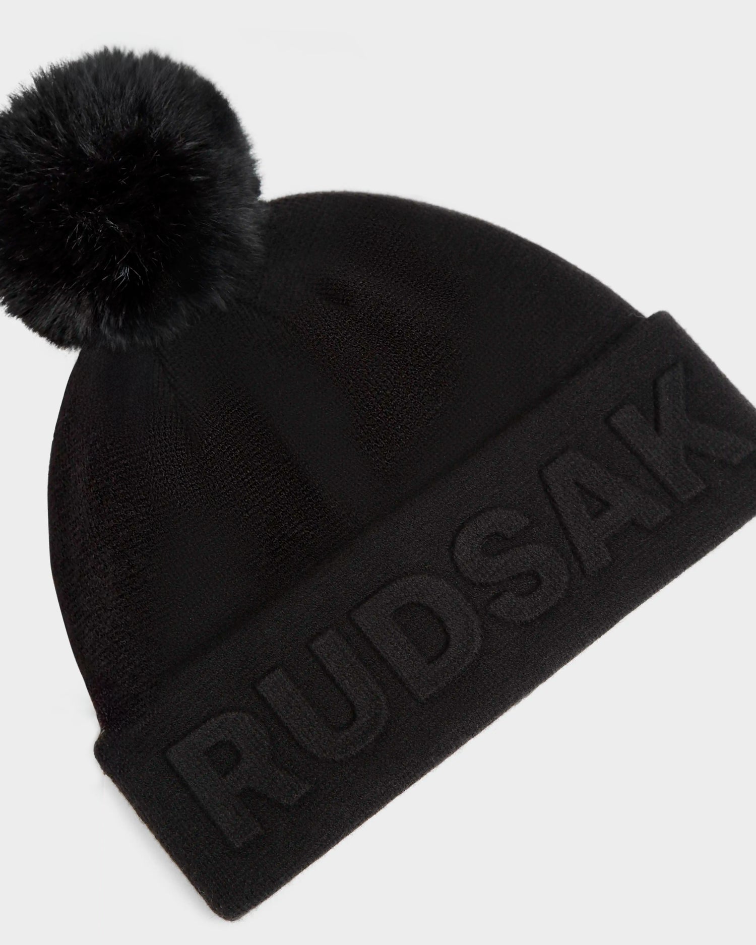 The CERRY - 9423508 Black by Rudsak is a unisex knit tuque featuring a large removable pom pom and bold Rudsak embroidery on the brim—a stylish wool beanie to keep you warm on chilly days.