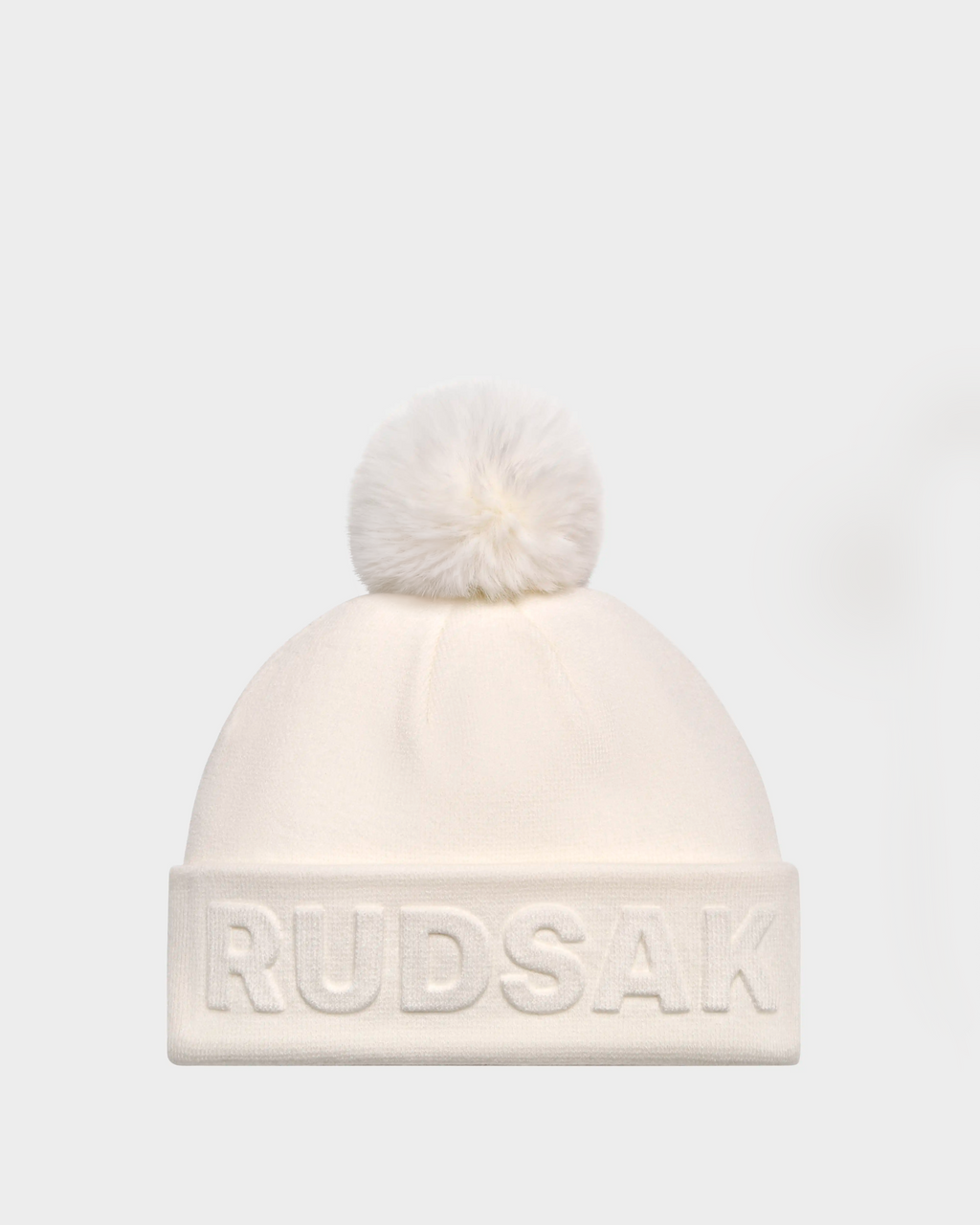 The CERRY - 9423508 Iceland is a white unisex knit tuque by Rudsak with a fluffy removable pom pom and RUDSAK embroidered on the folded cuff, shown against a plain light gray background.
