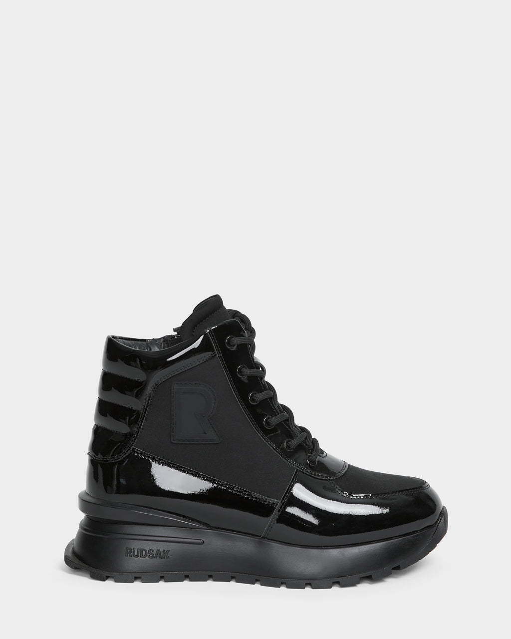 The CHELSA - L224505 Black by Rudsak is a women’s sneaker boot in black patent leather with a chunky sole, lace-up front, waterproof zipper, ribbed heel, and subtle side R logo. Glossy and weather-resistant for stylish wear.