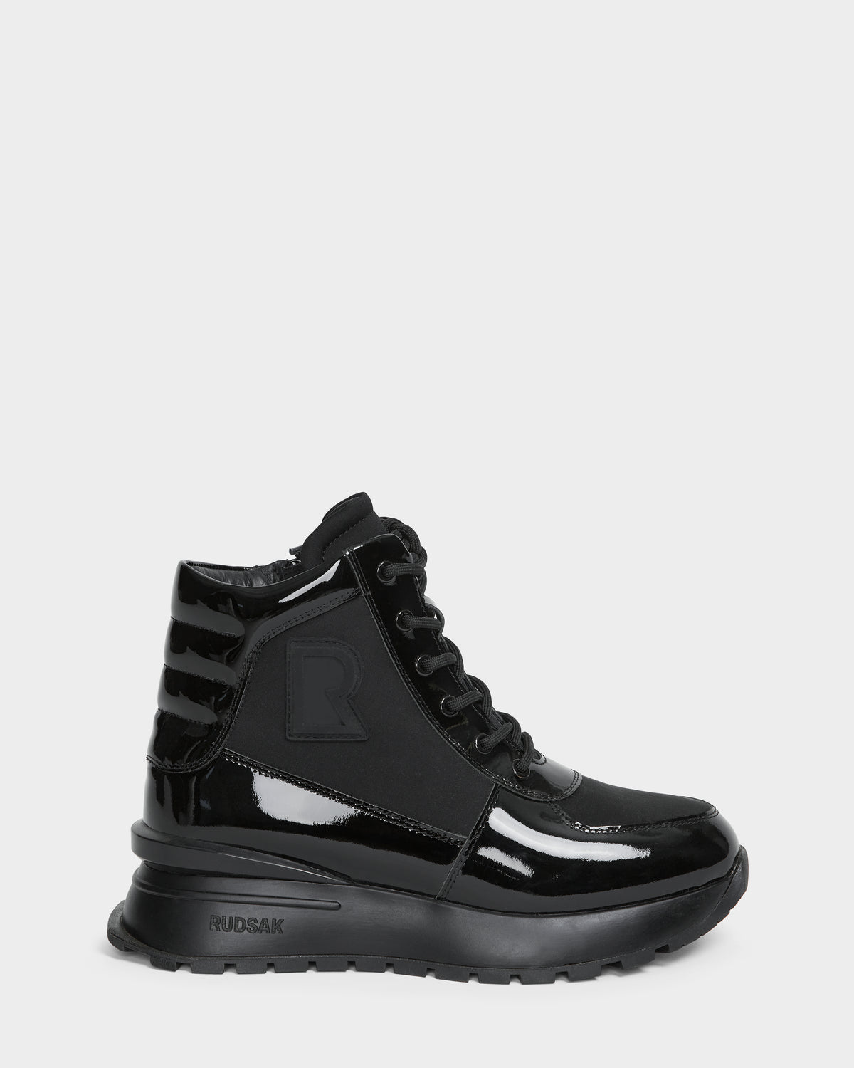 The CHELSA - L224505 Black by Rudsak is a women’s sneaker boot in black patent leather with a chunky sole, lace-up front, waterproof zipper, ribbed heel, and subtle side R logo. Glossy and weather-resistant for stylish wear.
