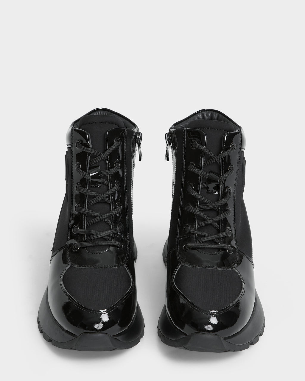 The Rudsak CHELSA - L224505 Black women’s sneaker boots feature glossy patent leather accents, lace-up fronts, and waterproof zipper sides, shown facing forward against a white background.