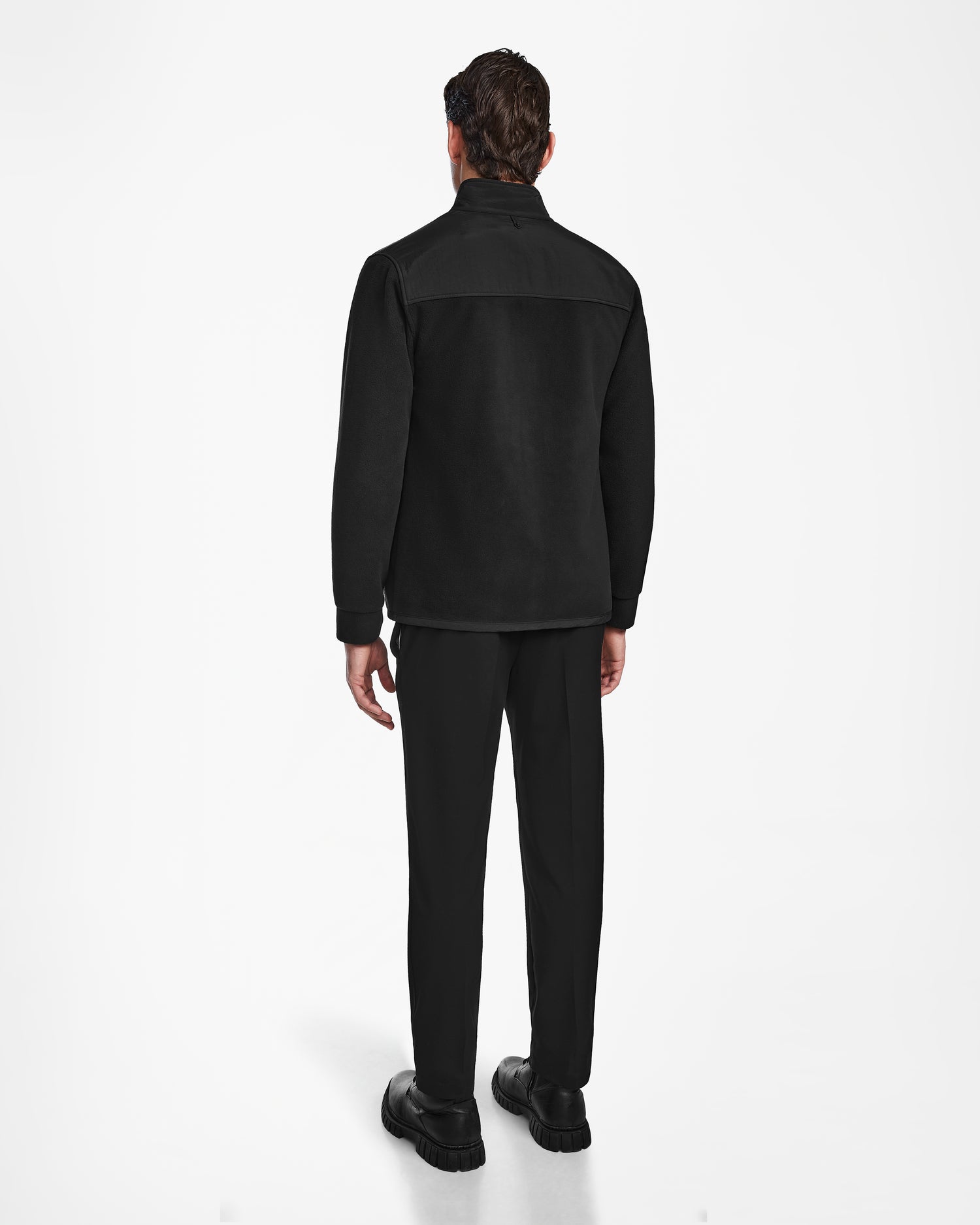 A man faces away from the camera against a white background, wearing Rudsak’s CHILIWACK - M524500 Black/Black polar fleece sweater, paired with black pants and black shoes.