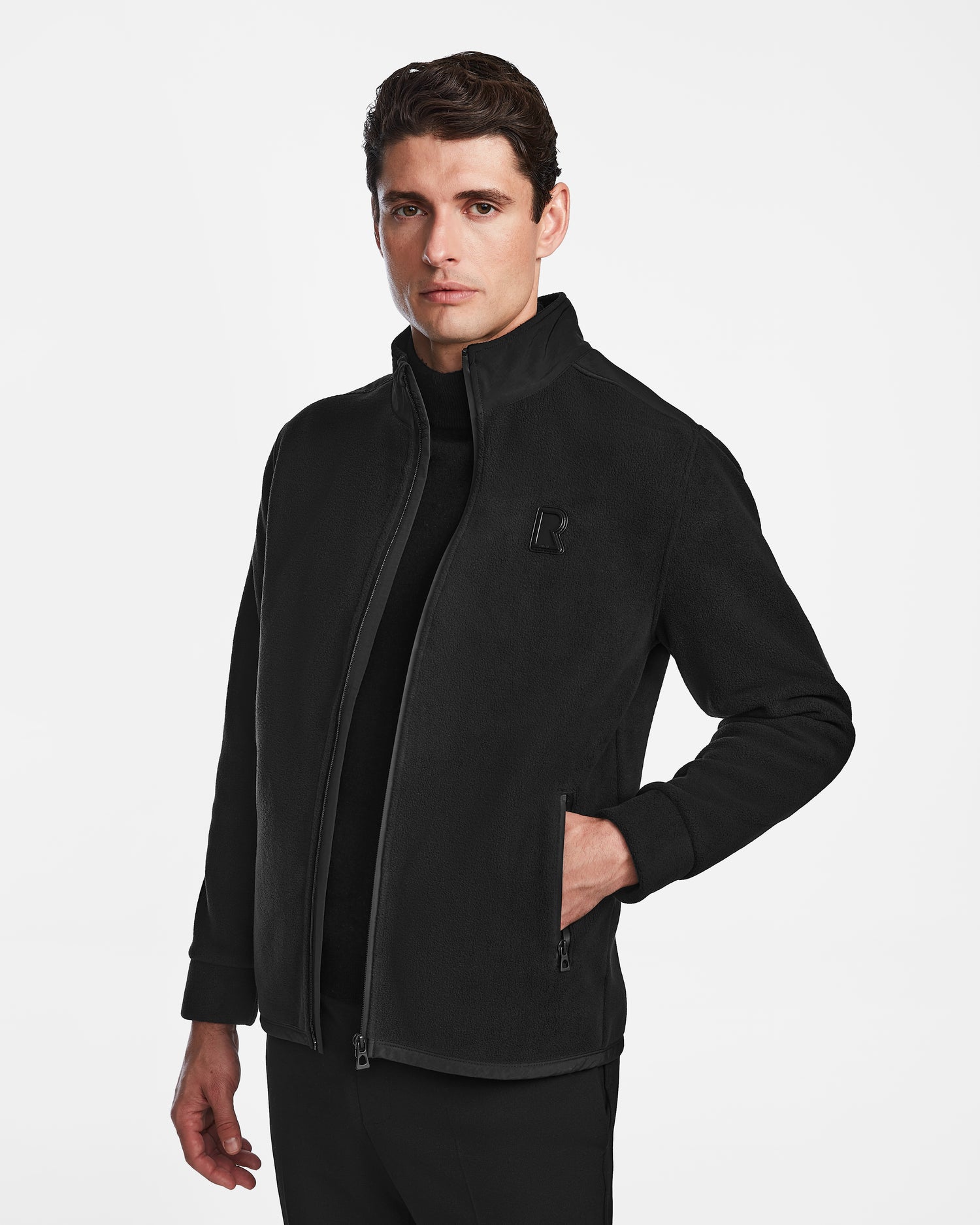 A man with short brown hair wears a Rudsak CHILIWACK - M524500 Black/Black men's polar fleece sweater, his left hand in the pocket, standing against a plain white background.