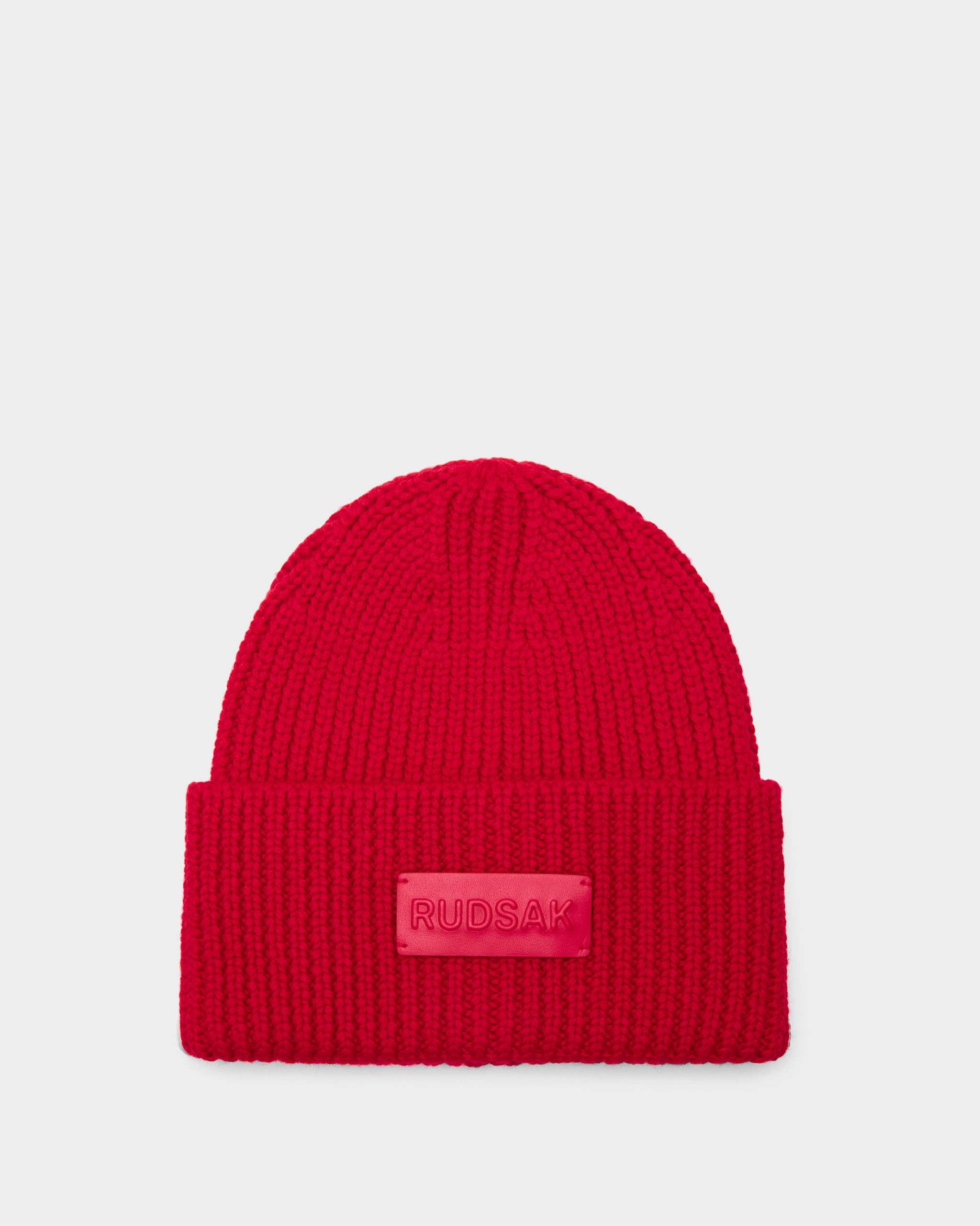 The COLIN - 9424518 Flame Red beanie by Rudsak is a bright red unisex hat featuring a wide folded brim and a rectangular RUDSAK patch on the front, shown against a plain light background.