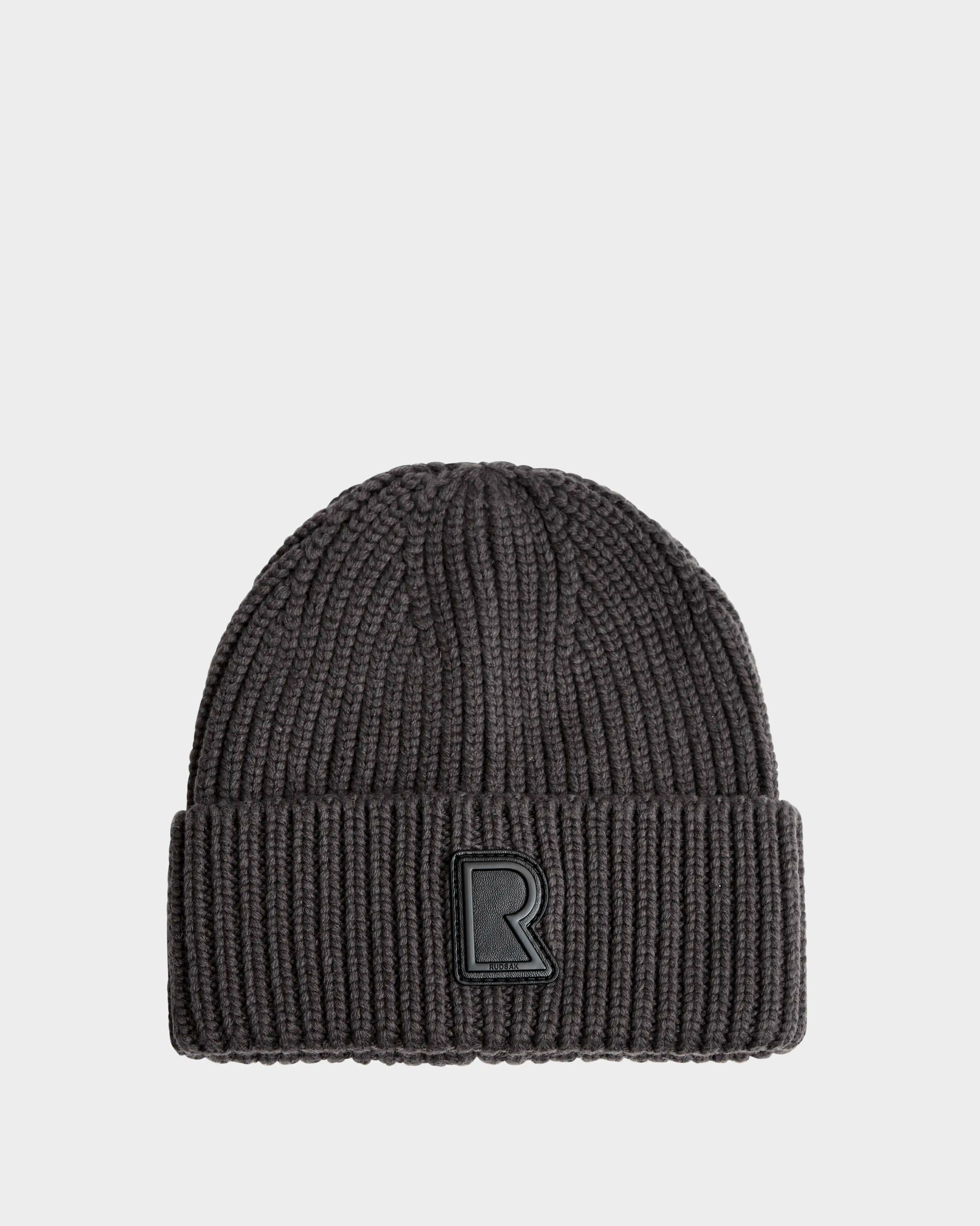 The CYBELLE - 9424504 Grey beanie by Rudsak is a dark gray ribbed wool blend hat with a folded brim and black R patch on the front, shown against a plain light background—a must-have unisex winter accessory.