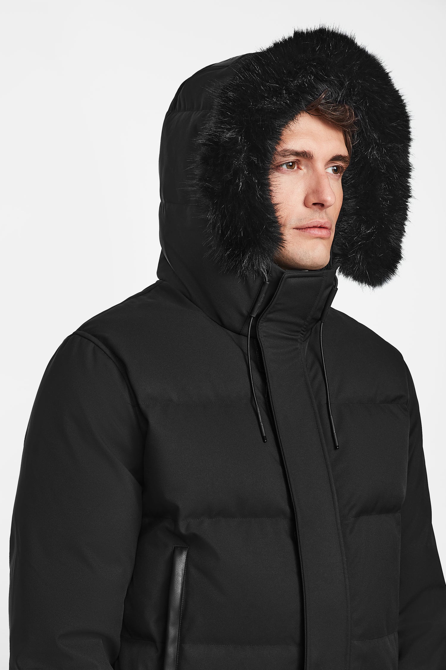 A man wears the Rudsak DALLAS - M122501 Black, a weather-resistant puffer coat with a fur-lined hood, looking to the side against a plain white background.