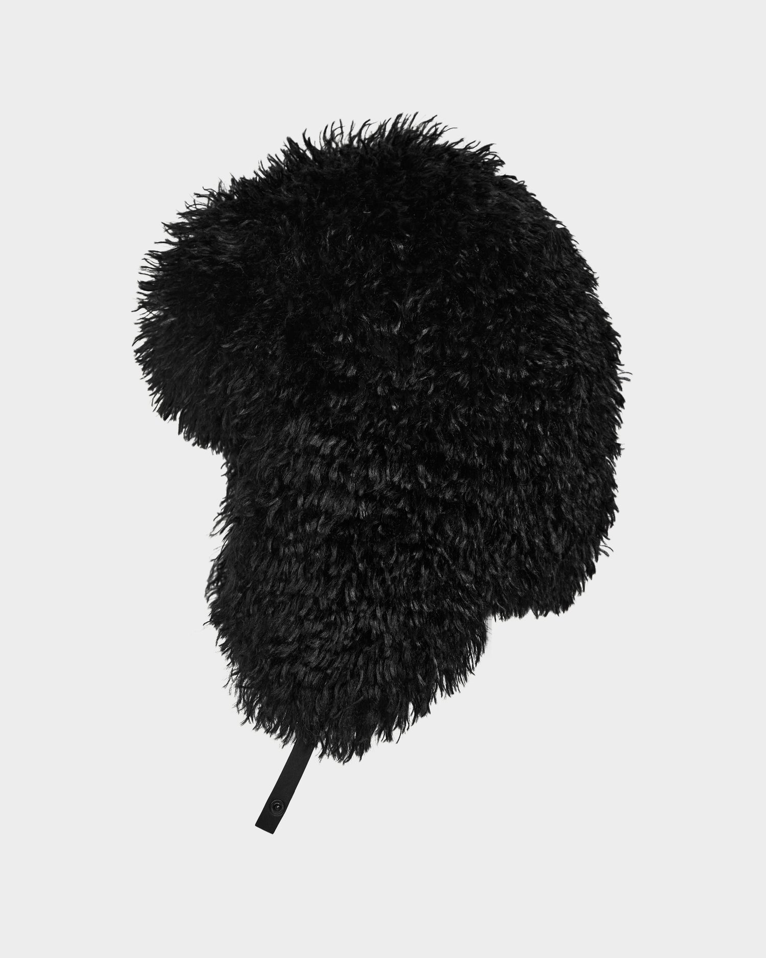 The DARBY M - 9424510 Black by Rudsak is a unisex aviator hat in black faux Mongolian fur with a fluffy, curly texture, rounded shape, and small bottom strap, shown on a plain light gray background.