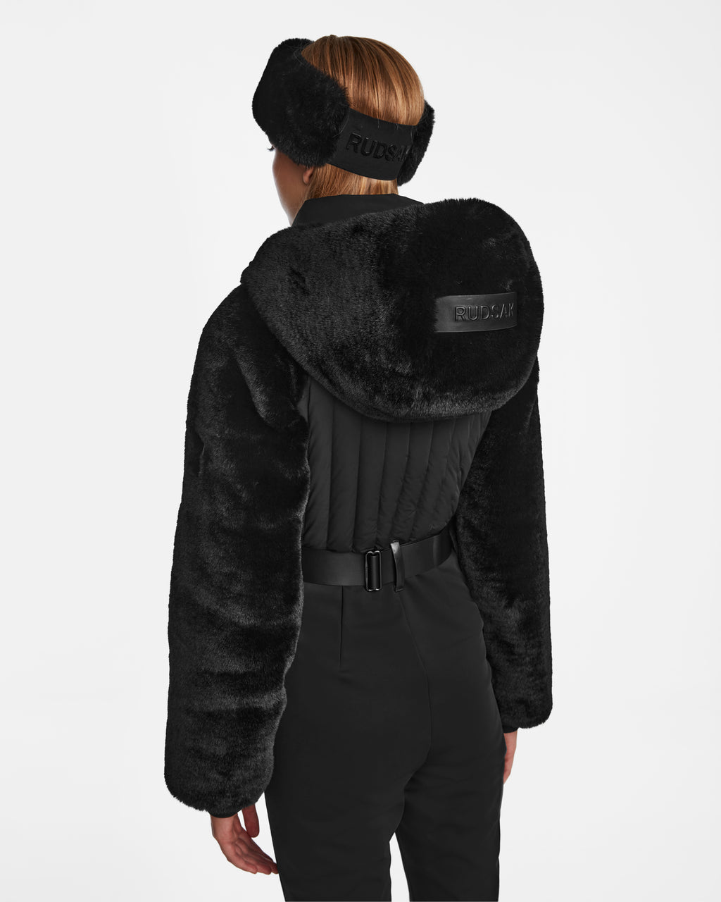 A person seen from behind wears Rudsak’s DESTINY - 8124727 Black faux fur hooded jacket and matching pants with a black fur headband, both featuring visible RUDSAK logos on the back—reminiscent of a women’s ski suit.