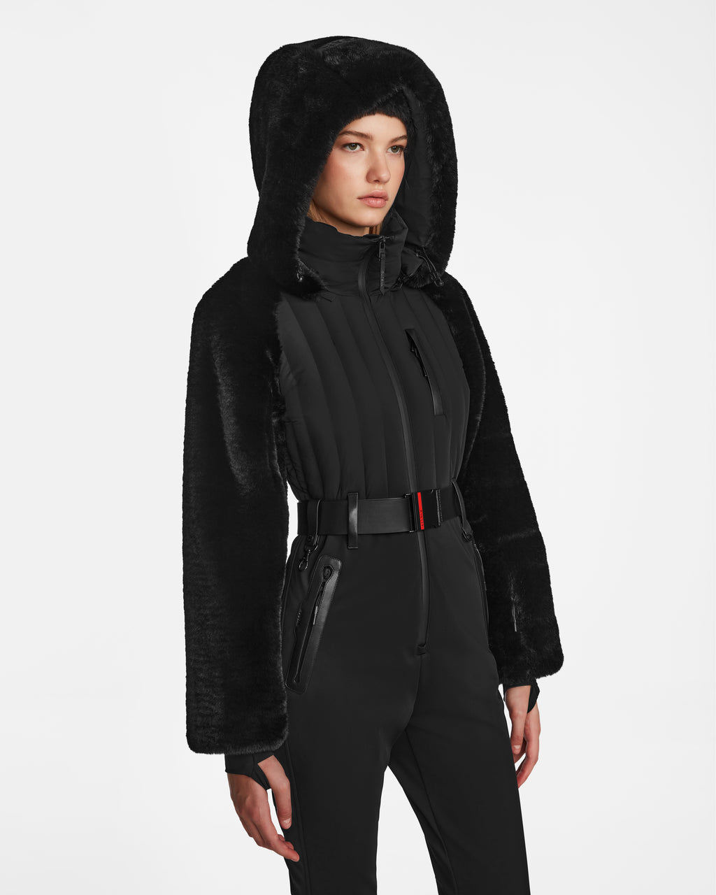 A woman models the Rudsak DESTINY - 8124727 Black jacket, featuring a belted waist, hood, faux fur sleeves, and padded front inspired by womens ski suits, against a plain white background.