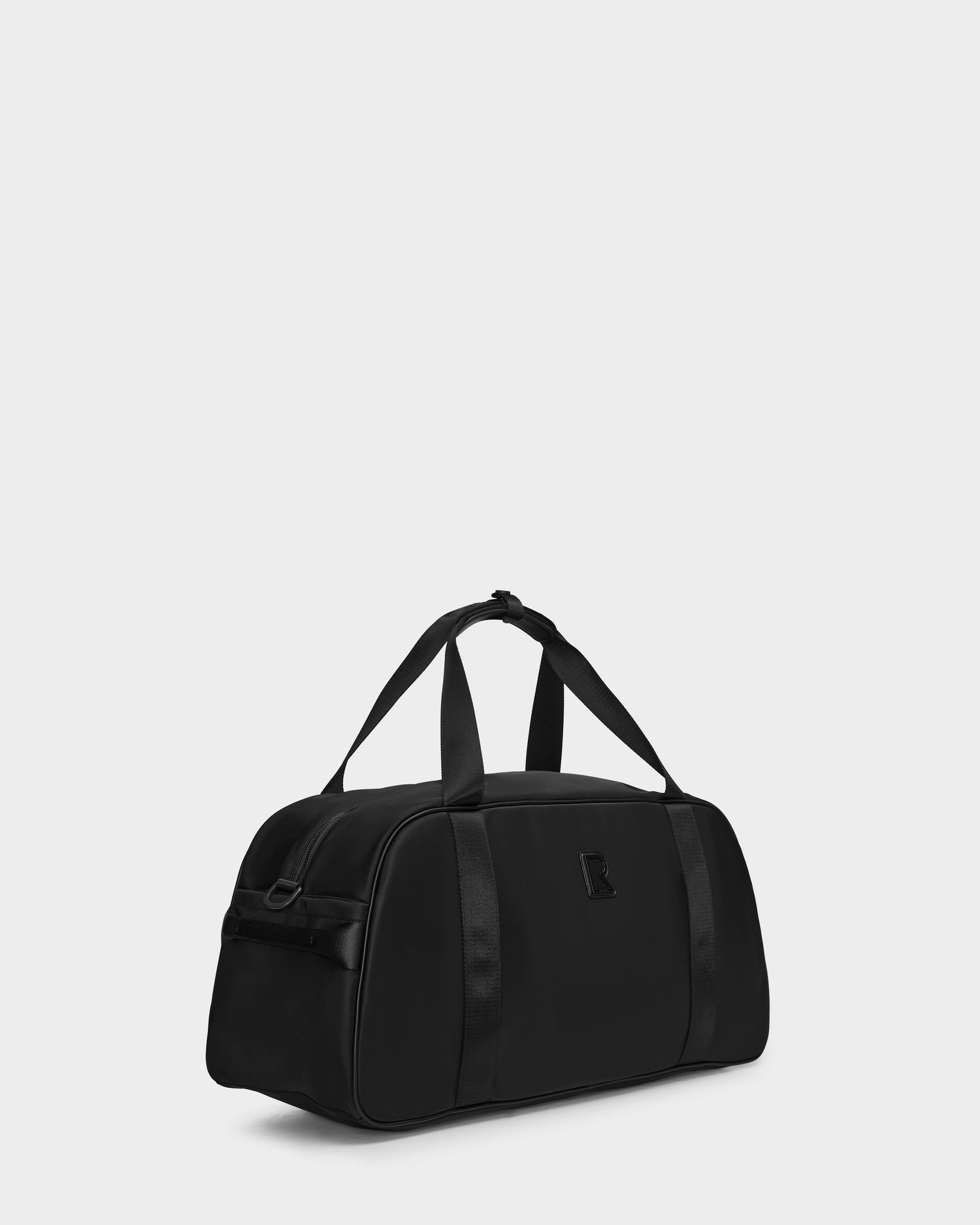 The Rudsak DUFF - 9324506 Black is a sleek unisex duffel bag with short handles and a detachable shoulder strap, featuring subtle black accents and a small logo—ideal for travel with style against a light gray backdrop.
