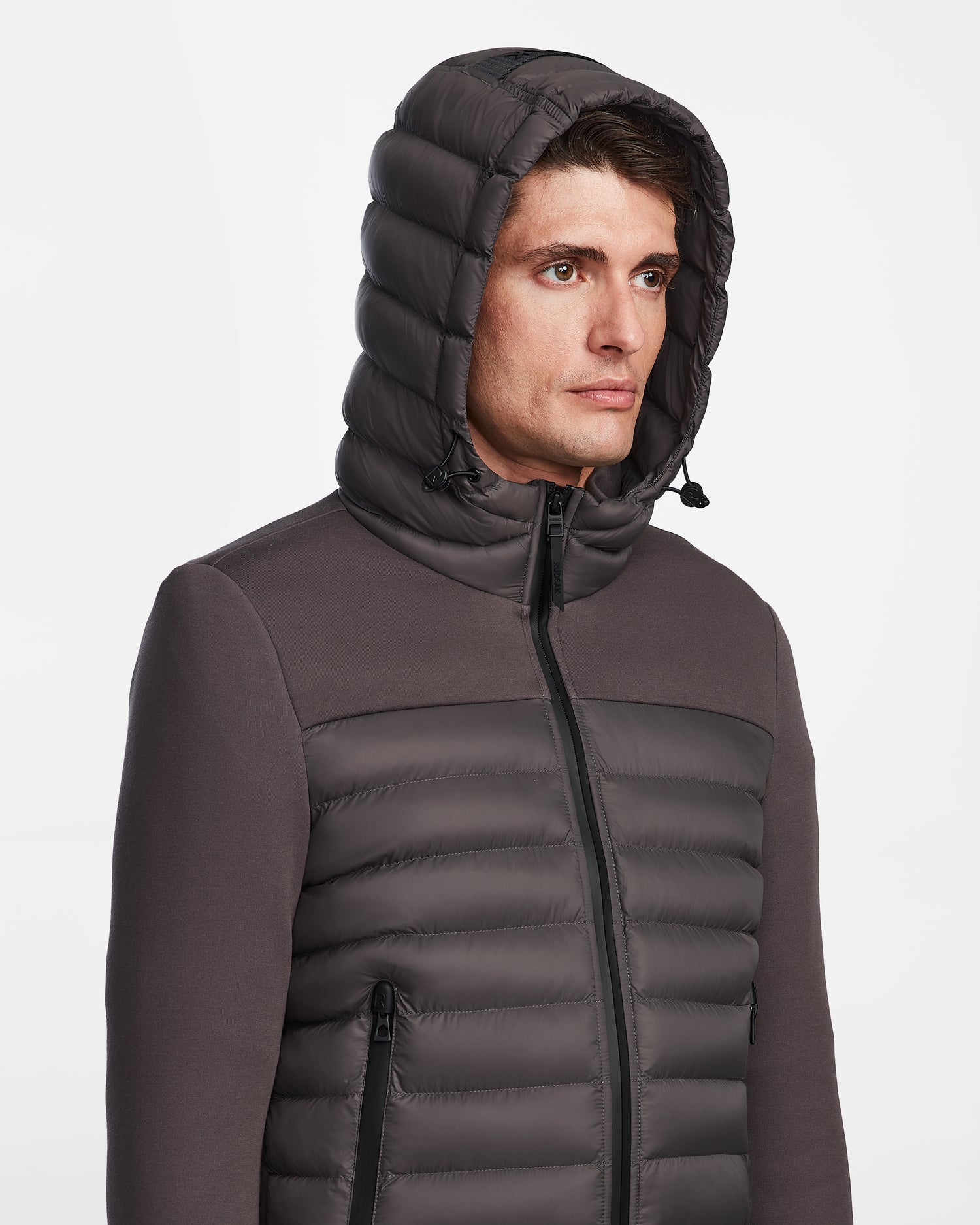 A man stands facing forward against a white background wearing the Rudsak DURIN M - M123515 Grey mens hooded jacket, featuring a front zipper, quilted design, and lightweight down insulation.