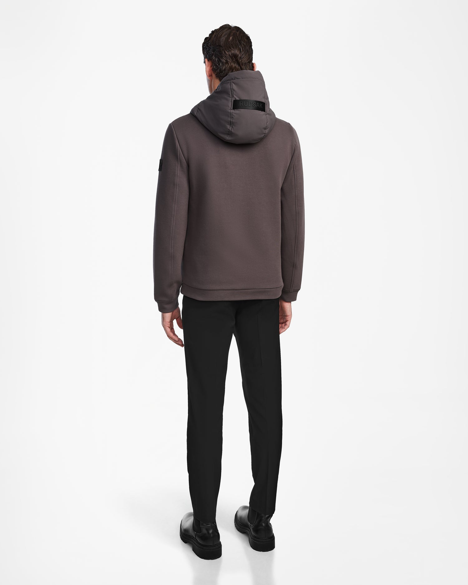 A man faces away from the camera wearing the Rudsak ELIAS - M124002 Grey men’s quilted light jacket, paired with black pants and shoes, against a plain white background.