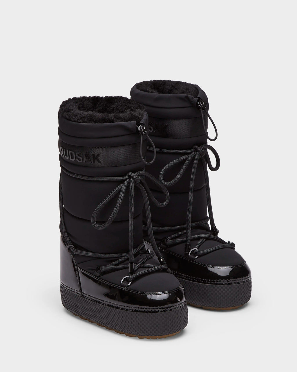 The Rudsak FARAH L - 8224542 Black boots feature black faux fur lining, shiny patent toe caps, thick platform soles, and lace-up fronts. Stylish and water-repellent, theyre perfect for staying warm on winter days. Displayed on a white background.