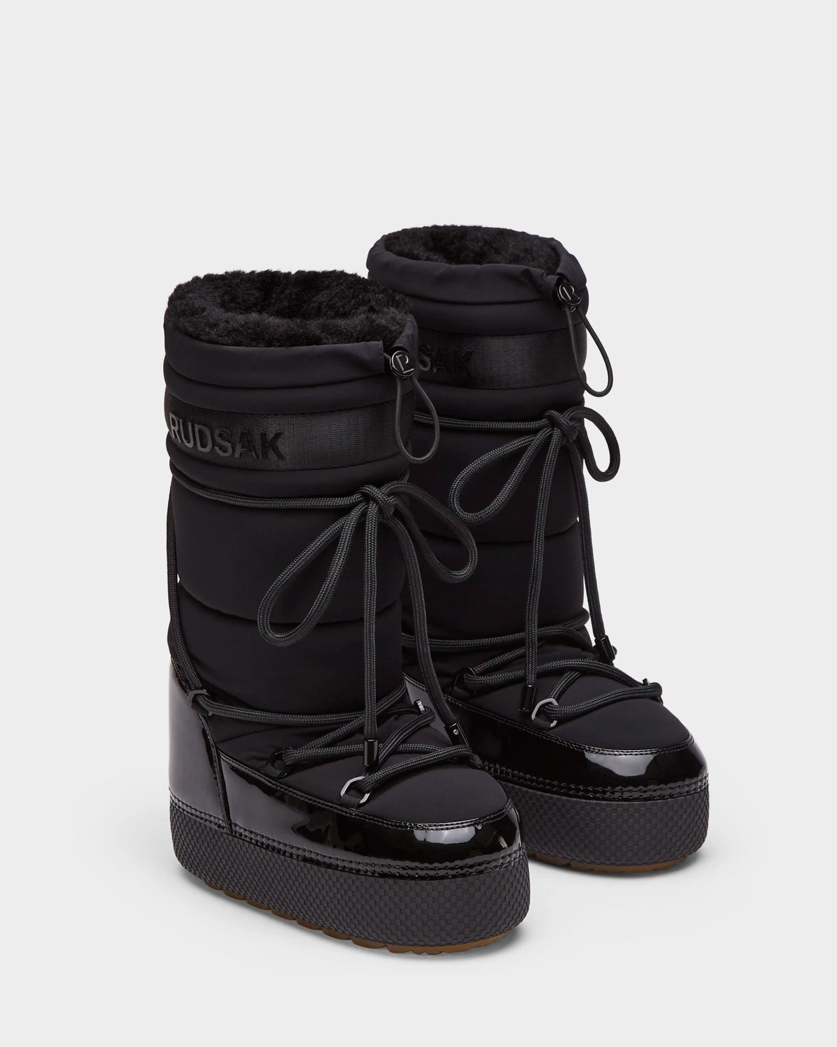 The Rudsak FARAH L - 8224542 Black boots feature black faux fur lining, shiny patent toe caps, thick platform soles, and lace-up fronts. Stylish and water-repellent, theyre perfect for staying warm on winter days. Displayed on a white background.