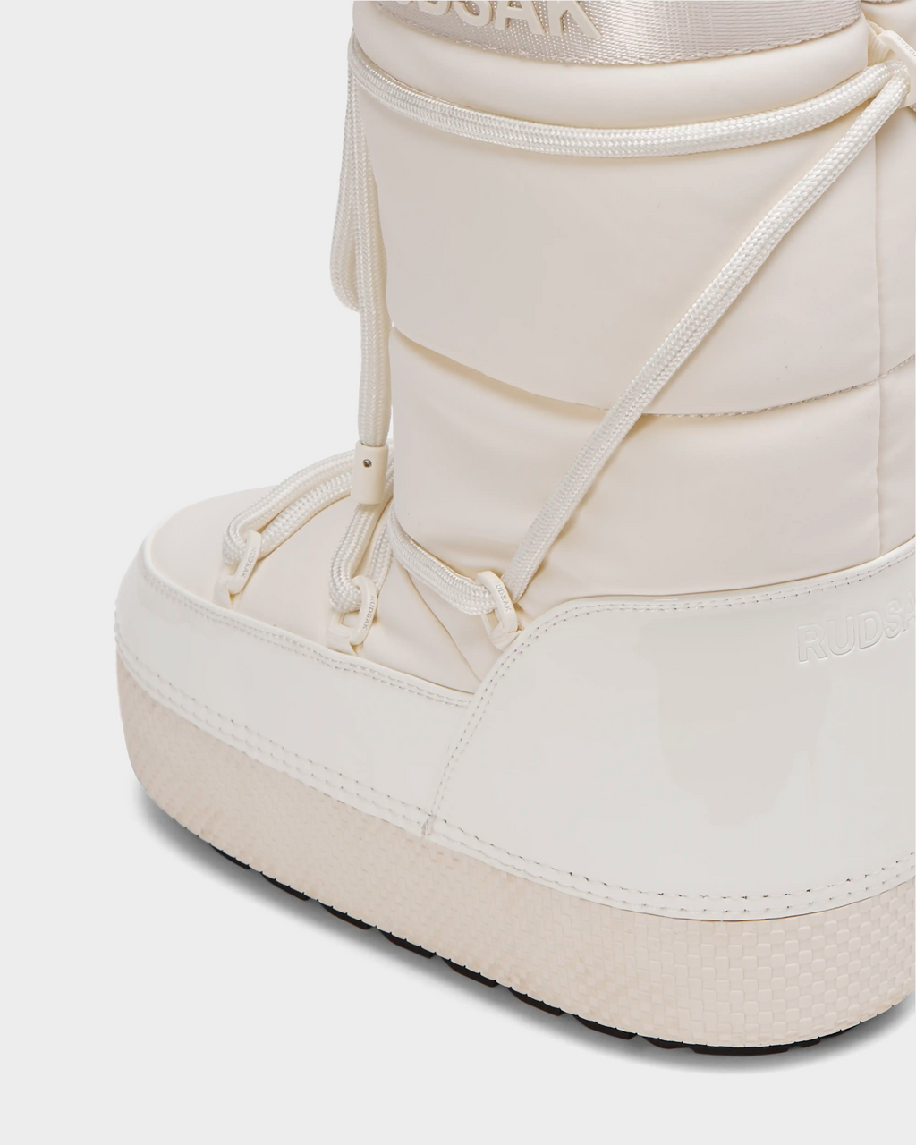 Close-up of the FARAH L - 8224542 Iceland by Rudsak: a white, shiny womens winter boot with water-repellent upper, thick textured sole, round toe, cord details, “RUDSAK” near the ankle, and faux fur lining for warmth.