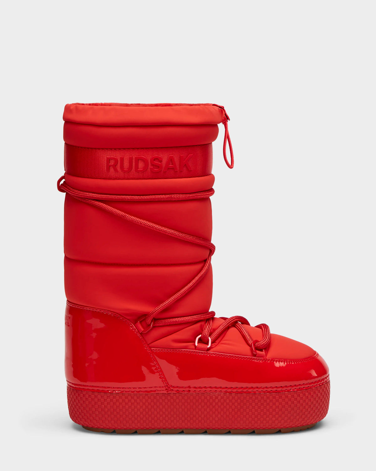 The FARAH - 8223501 Flame Red by Rudsak is a shiny, mid-calf winter boot with quilted padding, chunky sole, wraparound laces, water-repellent finish, faux fur lining for warmth, embossed branding near the top, and a zipper pull at the collar.