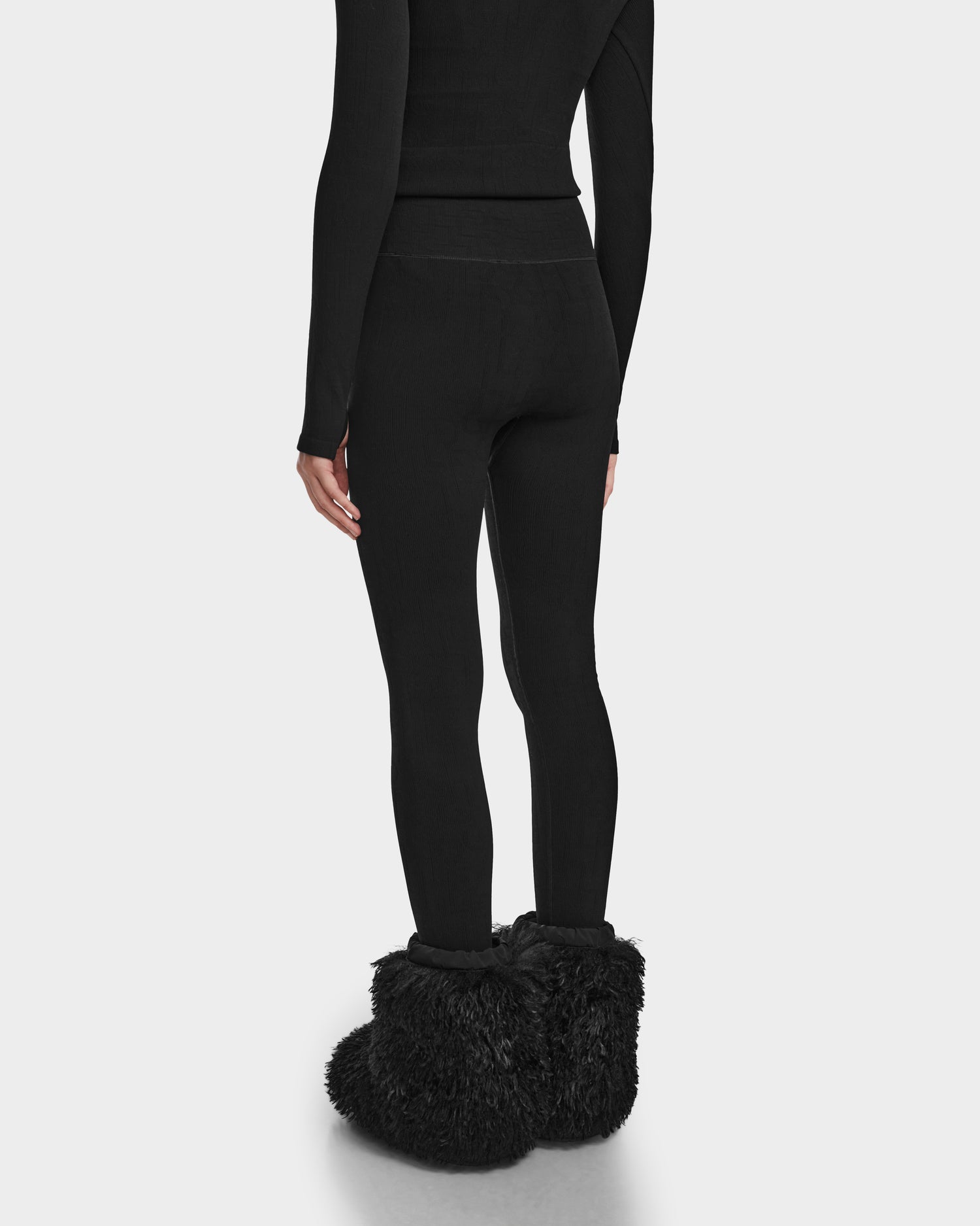 A person is shown from the back against a plain white background, wearing the Rudsak FERKA - 8524542 Monogram Print Black leggings—perfect for a cozy winter wardrobe.