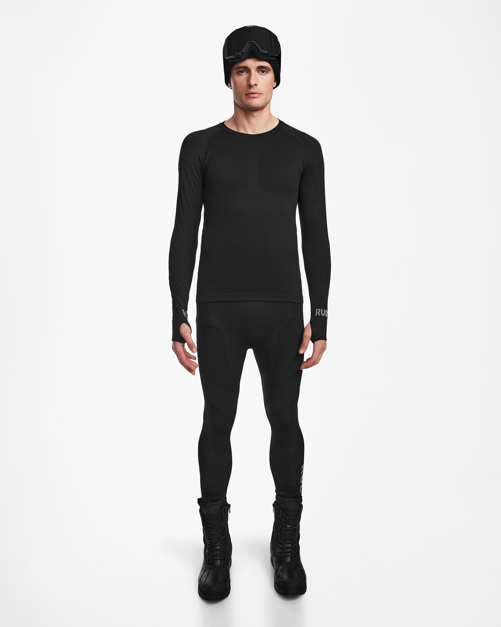 A man stands facing forward wearing the Rudsak FRANC - 6524541 Black fitted men’s thermal set with matching leggings, tall boots, and a black beanie with goggles, posed against a plain white background.