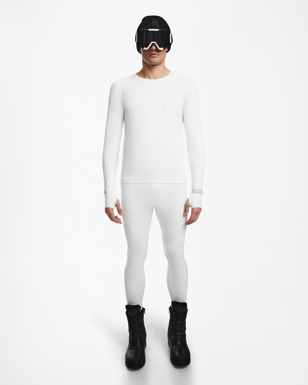 A person stands facing forward, wearing the Rudsak FRANC - 6524541 Iceland fitted white stretch base layer top and matching leggings, paired with black winter boots, ski goggles, and a beanie against a plain white background.