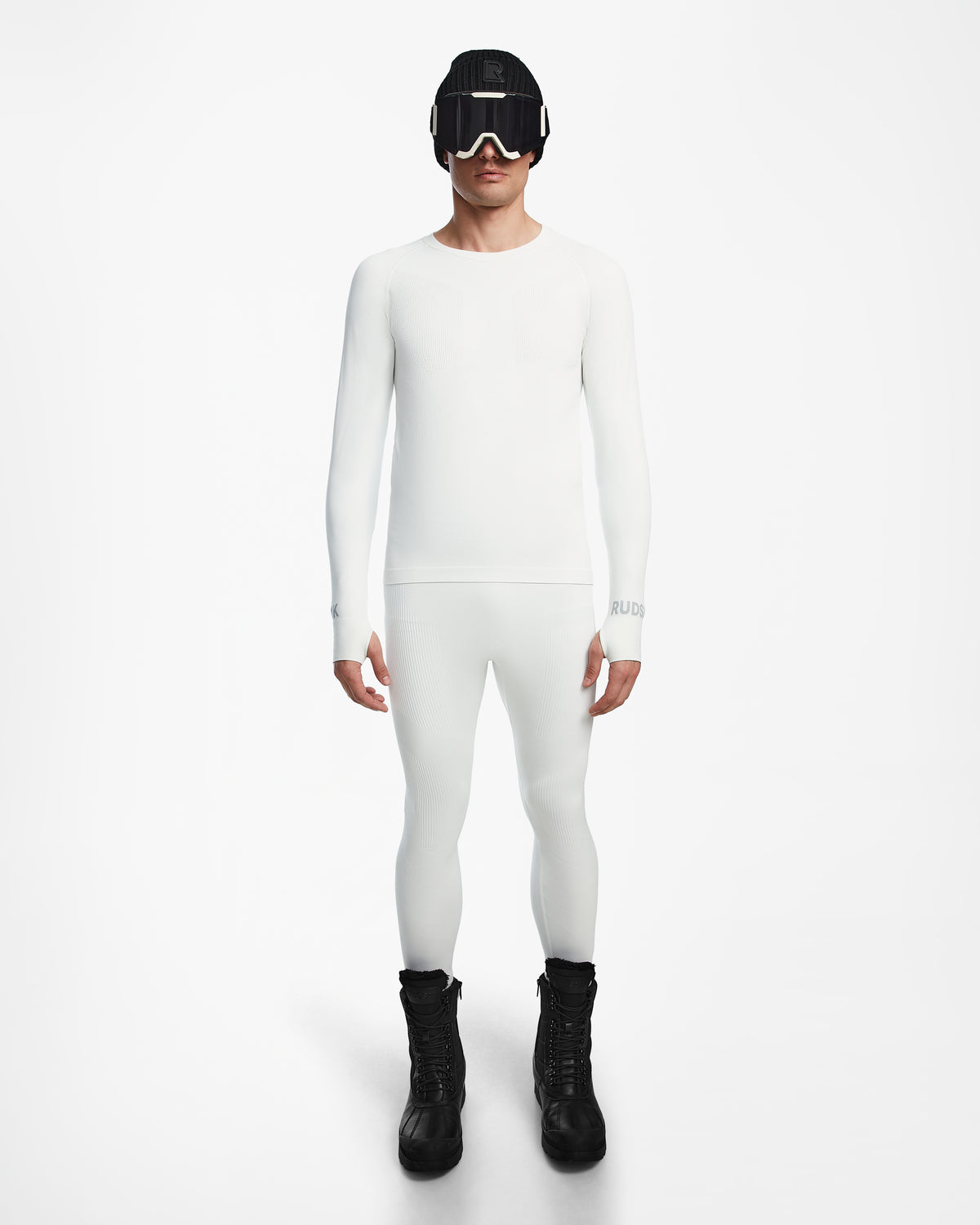 A person stands facing forward, wearing the Rudsak FRANC - 6524541 Iceland fitted white stretch base layer top and matching leggings, paired with black winter boots, ski goggles, and a beanie against a plain white background.
