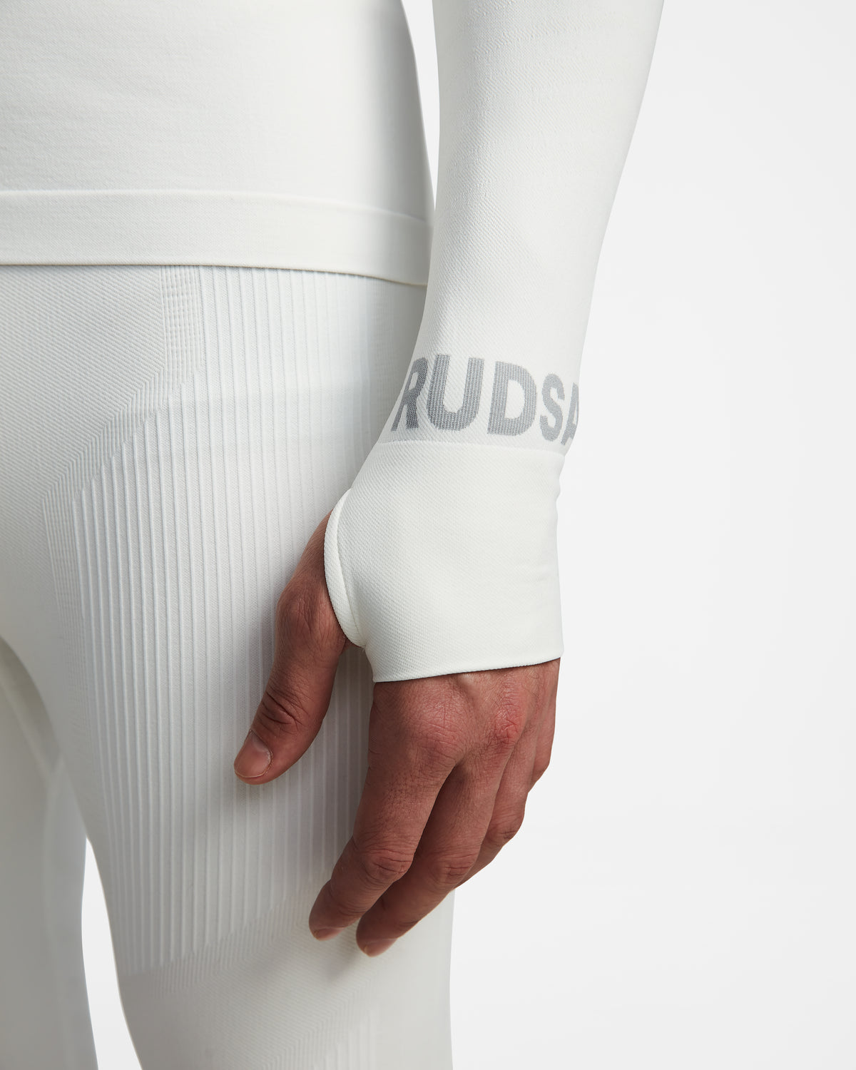 A person wears Rudsaks FRANC - 6524541 Iceland white long-sleeve stretch base layer and matching textured leggings, with a hand through the sleeve’s thumb hole and faint gray text near the wrist visible.