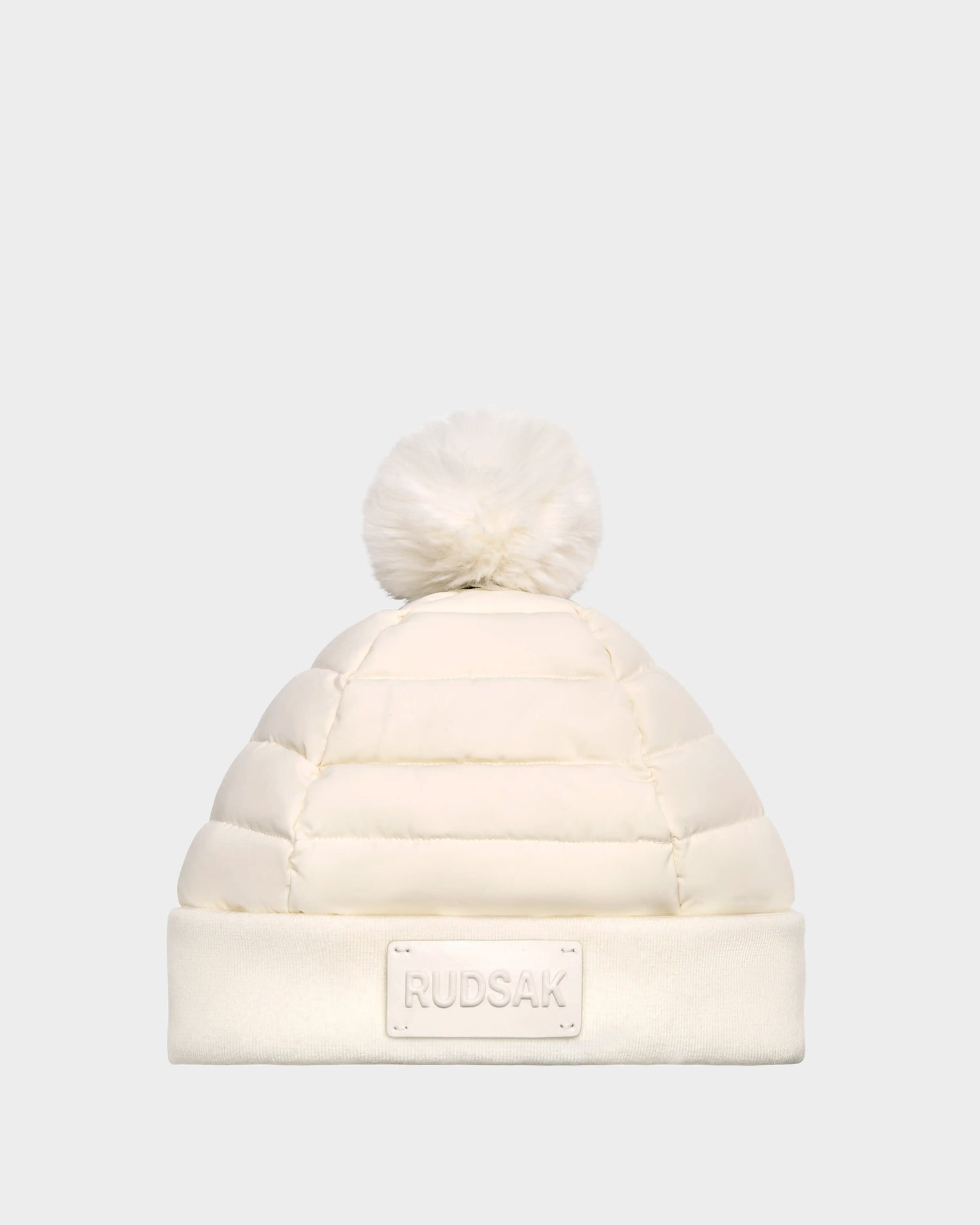 The GALA - 8424514 Iceland by Rudsak is a womens white quilted down puffer hat with a cozy folded brim, RUDSAK patch, and faux fur pom pom, shown on a plain light gray background.
