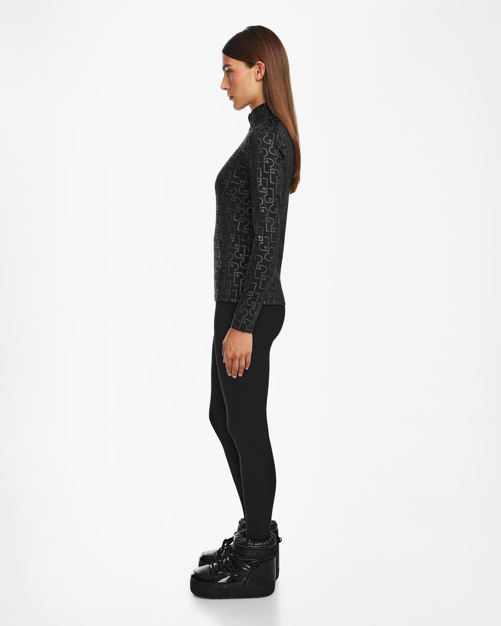 A woman in profile faces left, wearing the Rudsak GASIA - 8524567 black stretch active top with leggings and winter boots—perfect cold-weather activewear—set against a plain white background.