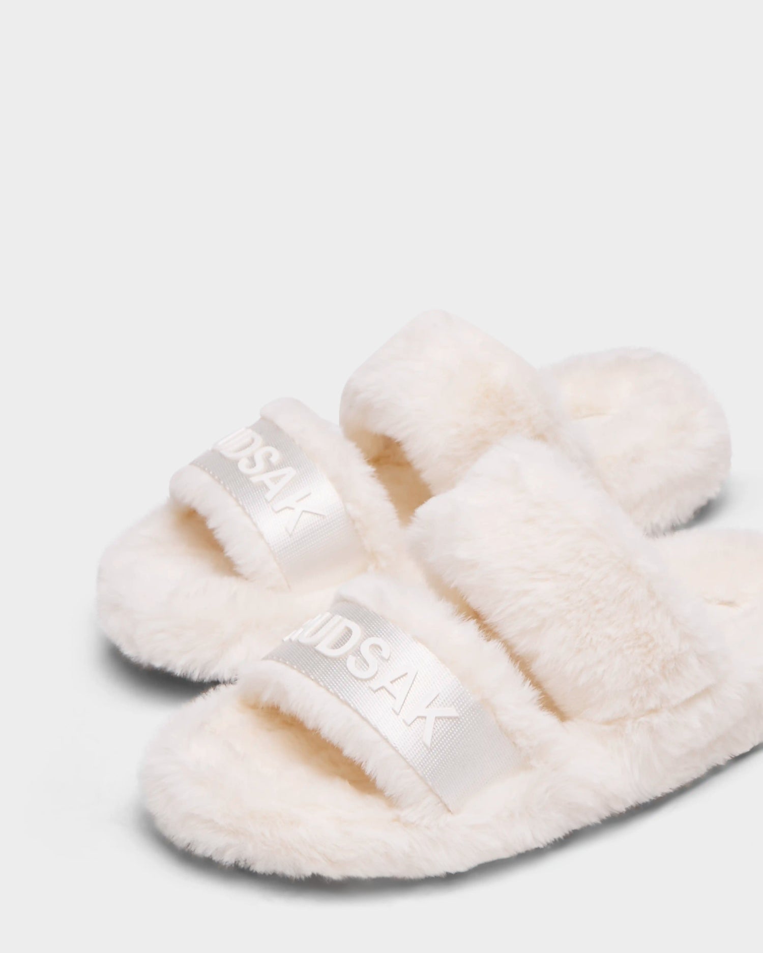 The GEMA - 8223510 Iceland by Rudsak are fluffy white women's faux fur slipper slides with two wide straps. "RUDSAK" is displayed on a white band, adding style to their soft, cozy texture for ultimate comfort.