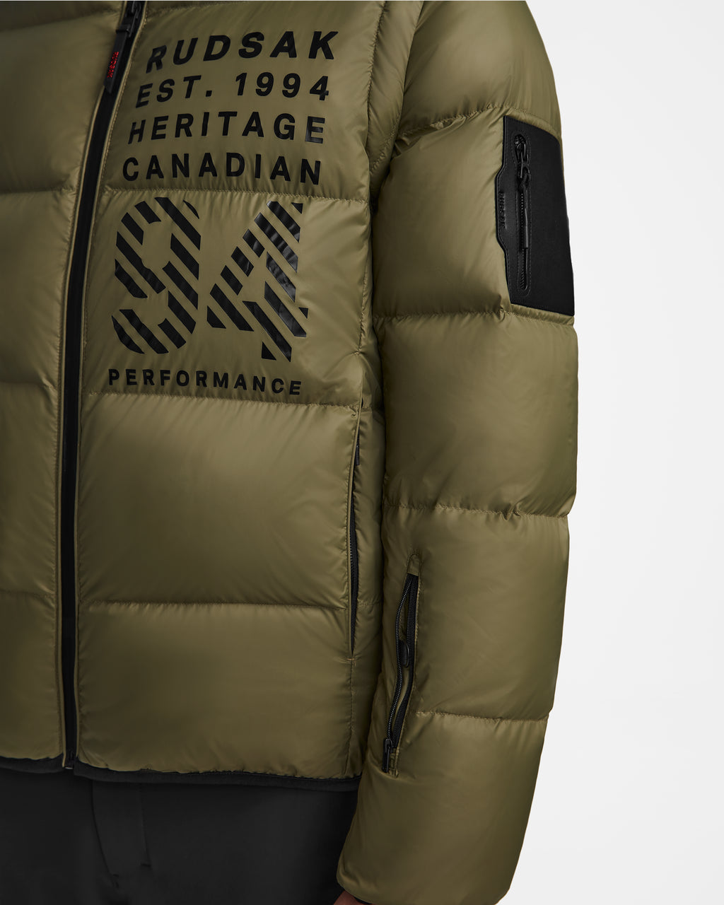 Close-up of the Rudsak HANS - 6124518 men’s ski jacket in Loden Green, featuring black zippers, “RUDSAK EST. 1994 HERITAGE CANADIAN 94 PERFORMANCE” chest text, wind and water resistance, and a sleeve zip pocket for utility.