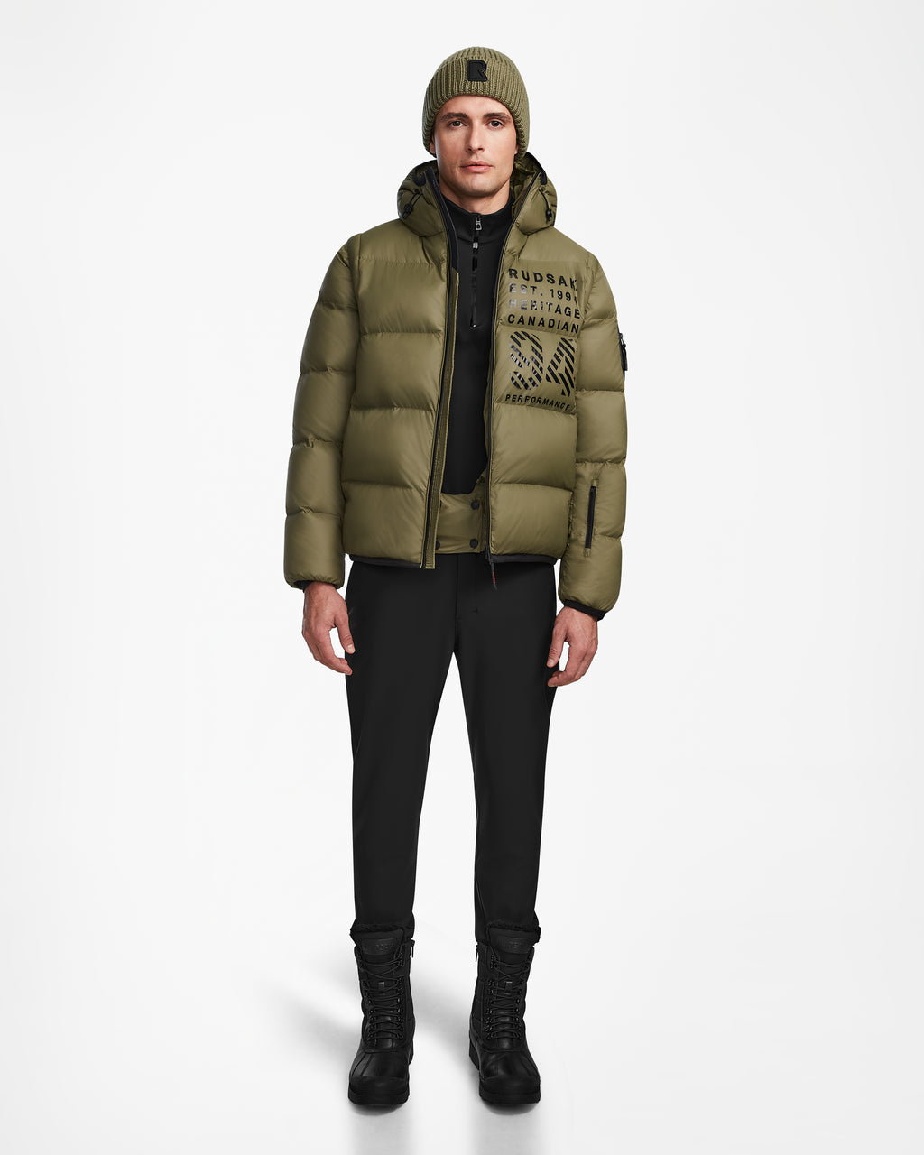 A person faces forward wearing the Rudsak HANS - 6124518 Loden Green men’s down ski jacket, a matching green beanie, black pants, and black boots against a plain white background.