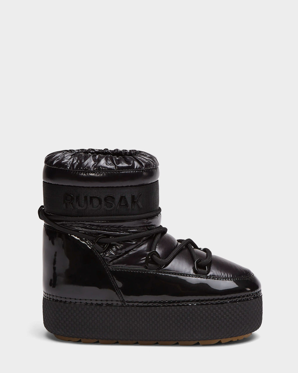 The HARLOW Y - 1223500 Black by Rudsak is a shiny black, high-top kid’s winter boot with a thick platform sole, quilted upper, wraparound laces, and a weather-resistant design featuring RUDSAK embossed on the ankle band.