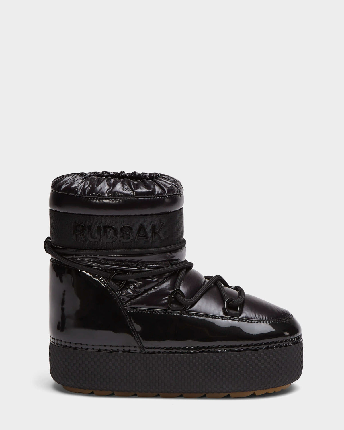The HARLOW Y - 1223500 Black by Rudsak is a shiny black, high-top kid’s winter boot with a thick platform sole, quilted upper, wraparound laces, and a weather-resistant design featuring RUDSAK embossed on the ankle band.