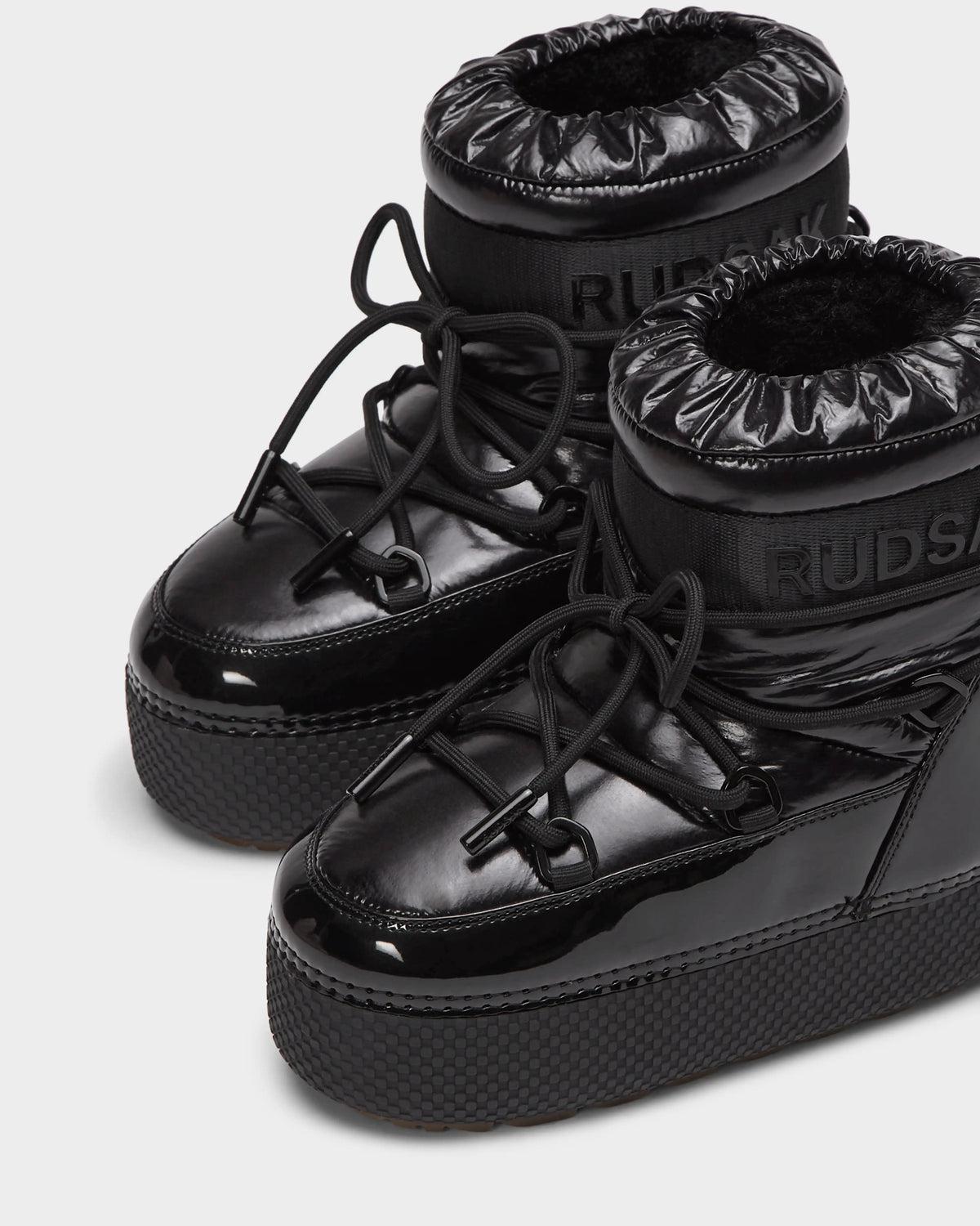 The HARLOW Y - 1223500 Black boots by Rudsak feature shiny, weather-resistant material, thick soles, puffy ankle cuffs, and crisscross laces—perfect stylish and comfy winter boots for kids.