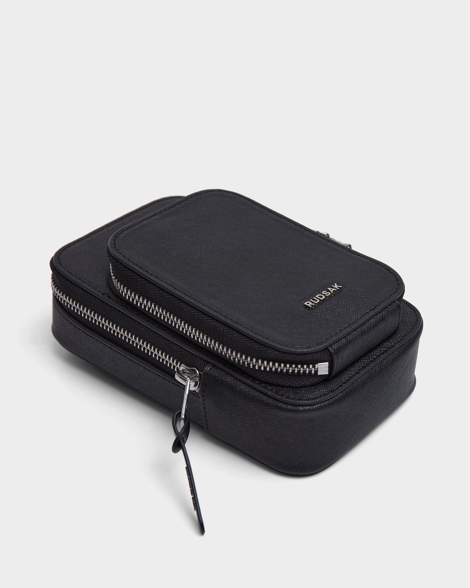 The Rudsak JIMIE - L324505 Black is a black, rectangular pouch featuring silver zippers, a small top zippered compartment with RUDSAK embossed in silver, all set against a white background.