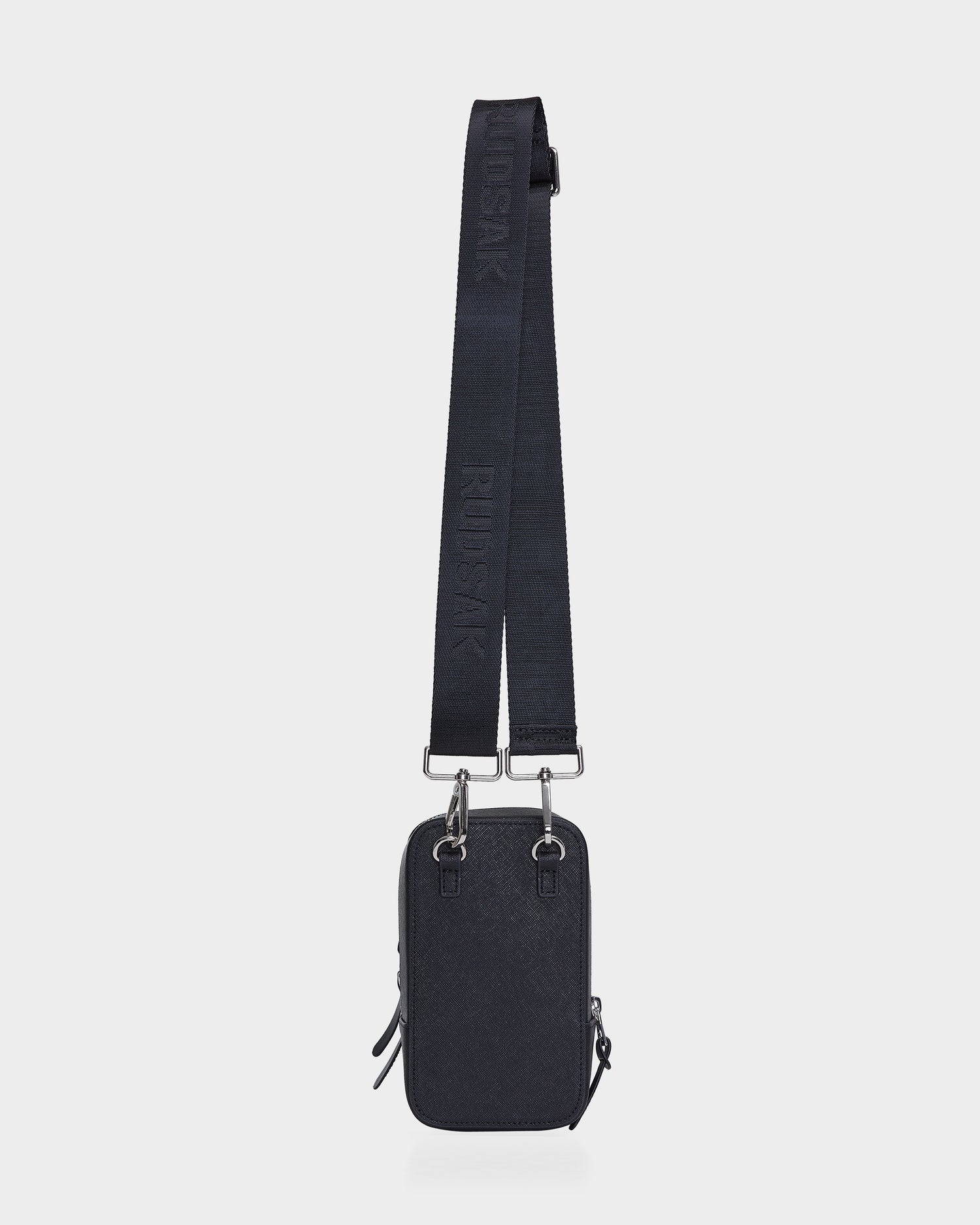 The JIMIE - L324505 Black by Rudsak is a small, rectangular black crossbody bag with silver hardware, a wide adjustable embossed strap, minimalist design, and zippered closure.