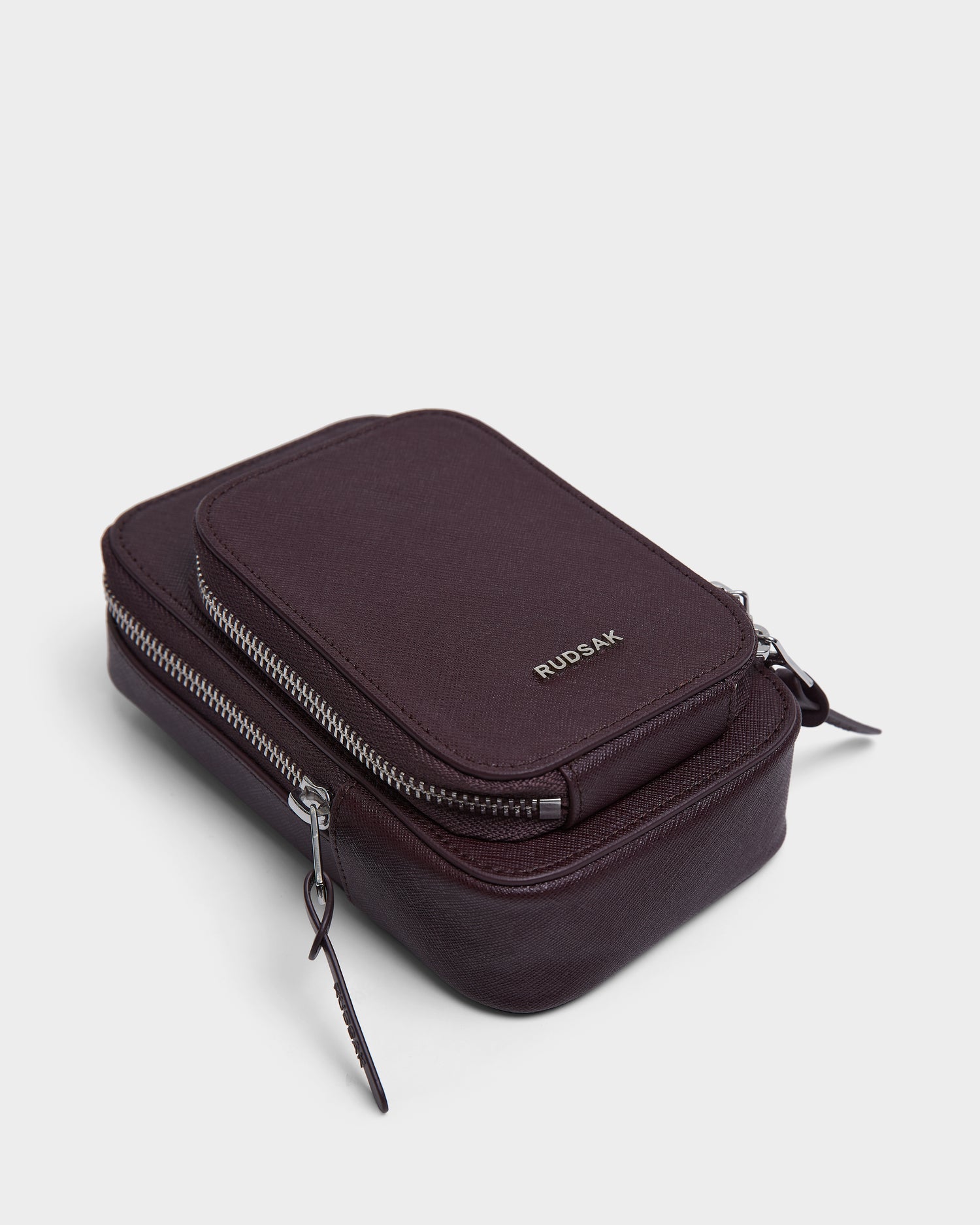 A compact, rectangular wine-colored leather pouch with two zippered compartments and Rudsak embossed in silver on the front. The JIMIE - L324505 is shown against a plain white background.
