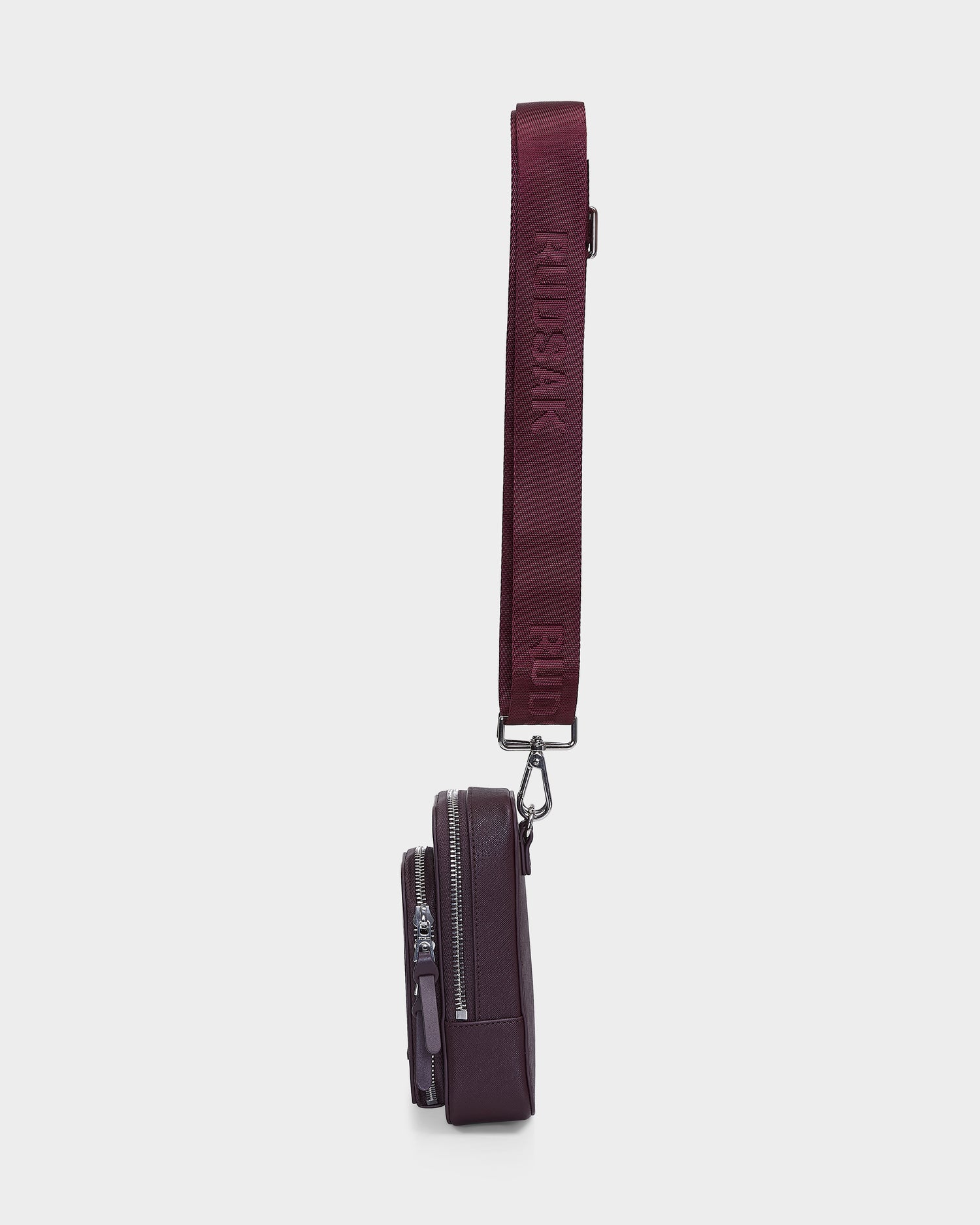 Side view of the Rudsak JIMIE - L324505 Wine crossbody bag featuring two zippered compartments and a wide adjustable strap embossed with RUDSAK, set against a plain white background.