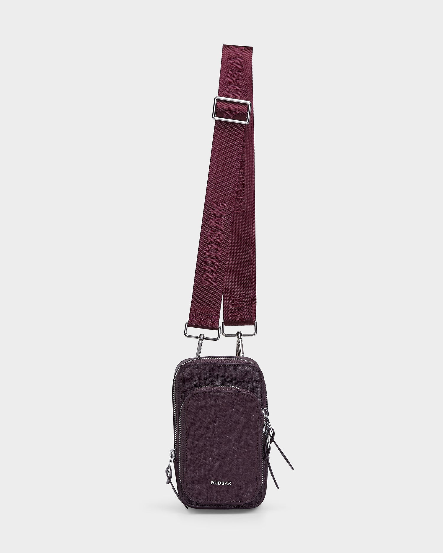 The JIMIE - L324505 Wine by Rudsak is a small, rectangular burgundy crossbody bag with two zippered compartments, silver hardware, and an adjustable strap embossed with the Rudsak brand name.