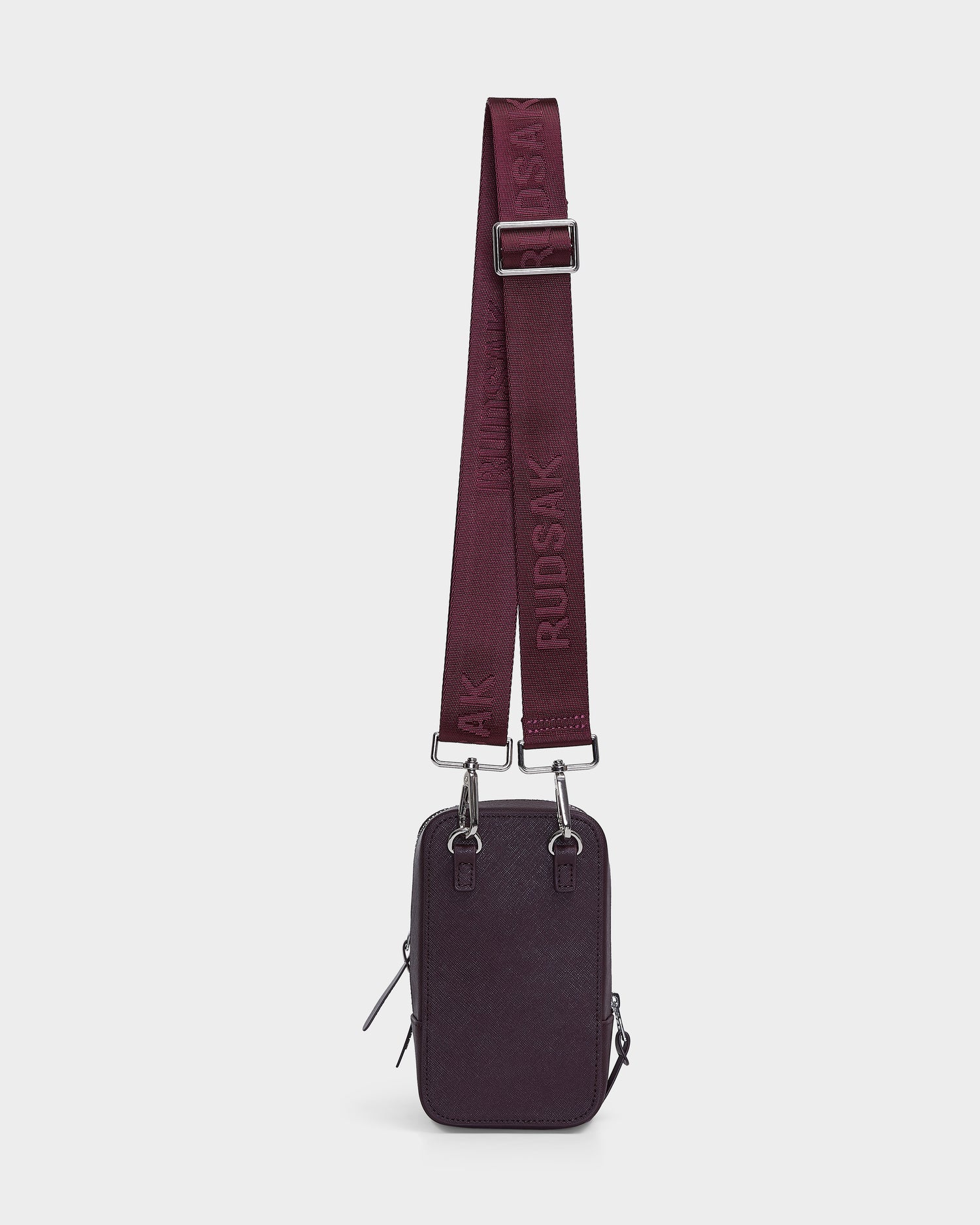 The JIMIE - L324505 Wine by Rudsak is a small, rectangular dark purple crossbody bag with a wide adjustable burgundy strap embossed with RUDSAK, two zippers, and silver hardware, shown on a plain white background.