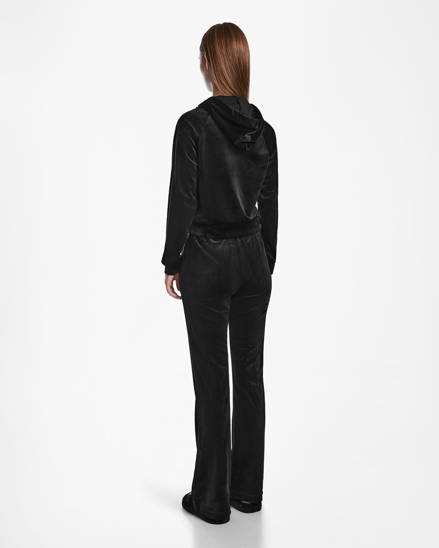 A person with straight, long hair faces away, wearing the Rudsak JODIE - L523501 Black velour hoodie and women’s velvet pull-on pants with an elastic waistband against a white background.